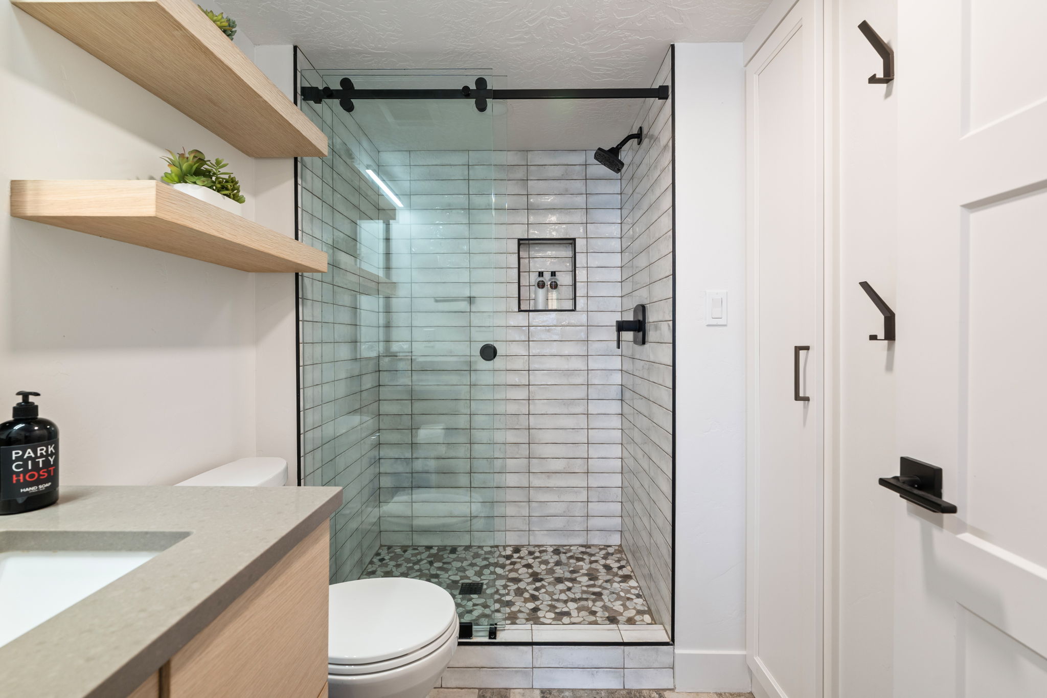 Glass-enclosed shower with subway tile surround and pebble-style flooring