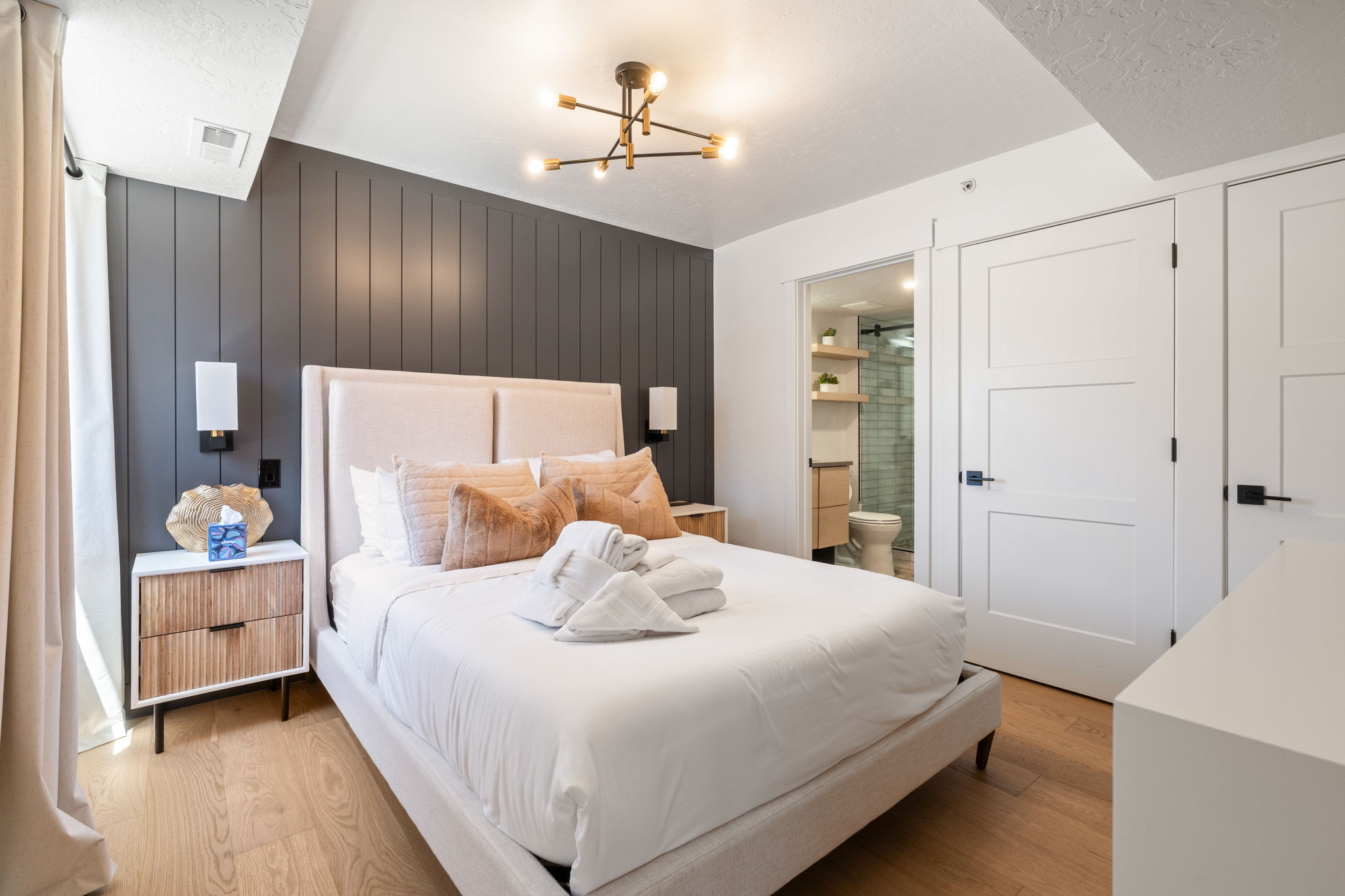 Bedroom featuring a paneled accent wall, wood-finish flooring, and a modern ceiling light fixture