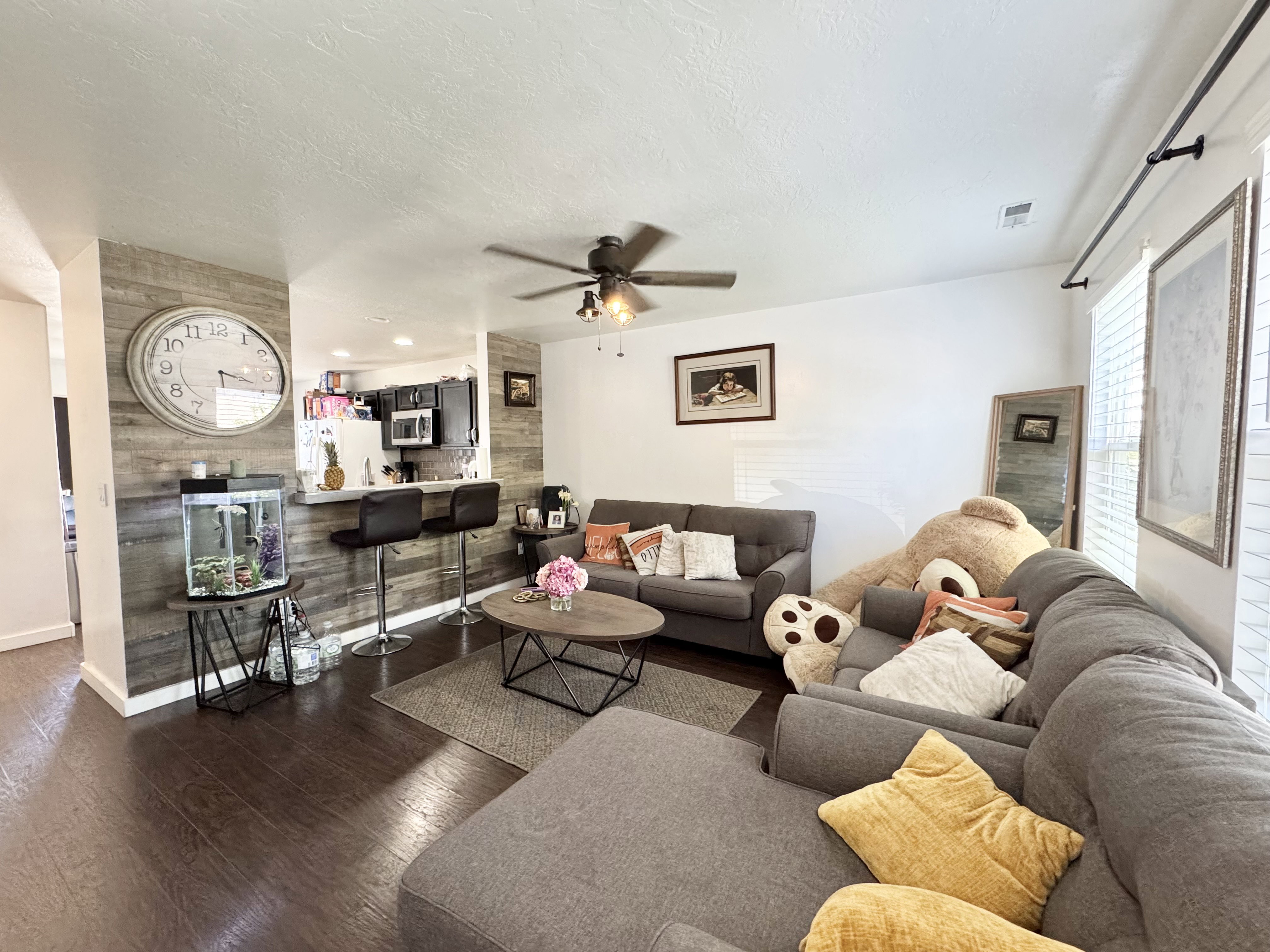 Open-concept living area featuring wood-finish flooring, a contemporary ceiling fan, and a breakfast bar with two stools