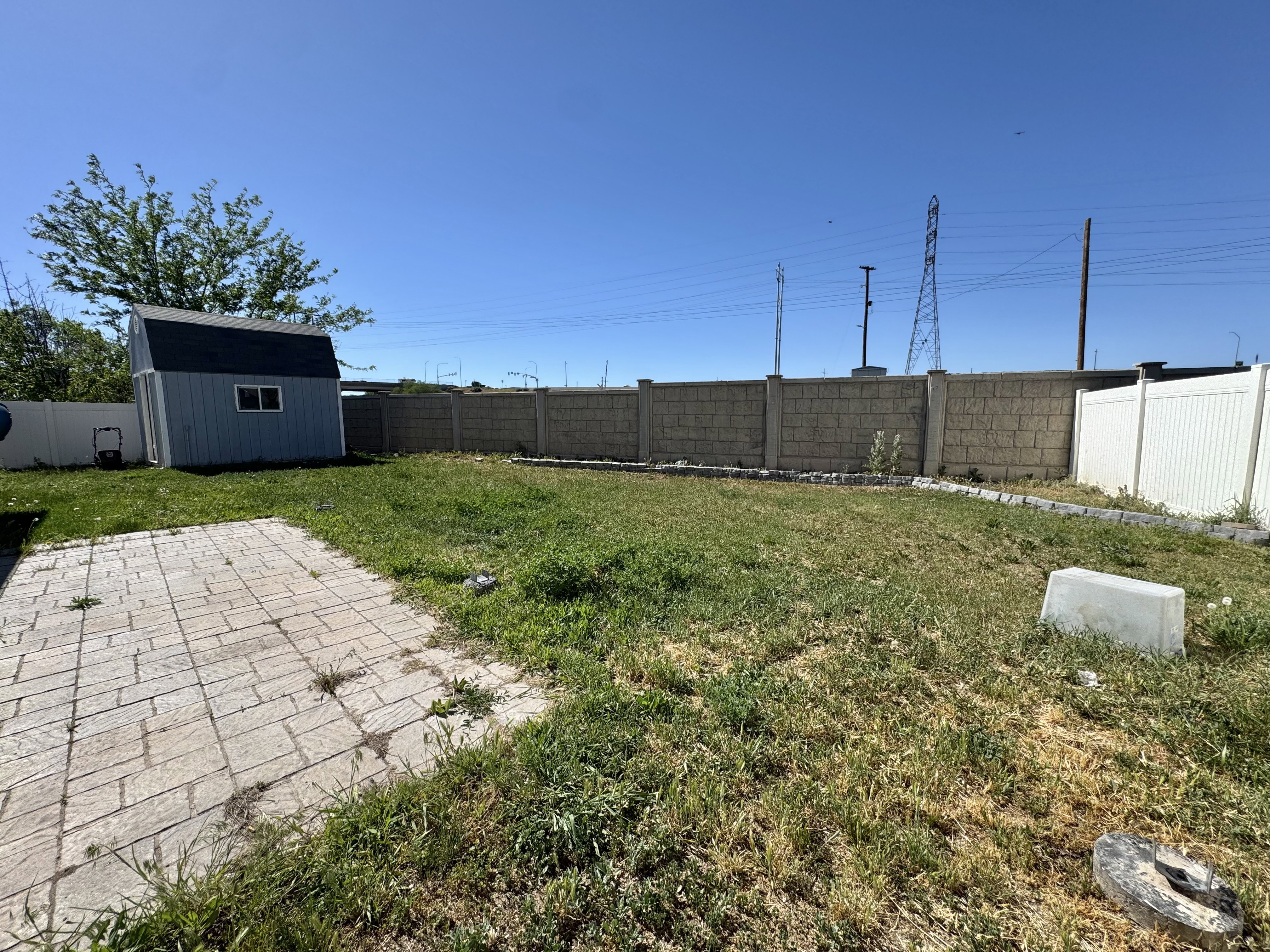 Expansive backyard featuring a stone paver patio, a light blue storage shed with white trim, and a combination of block and privacy fencing