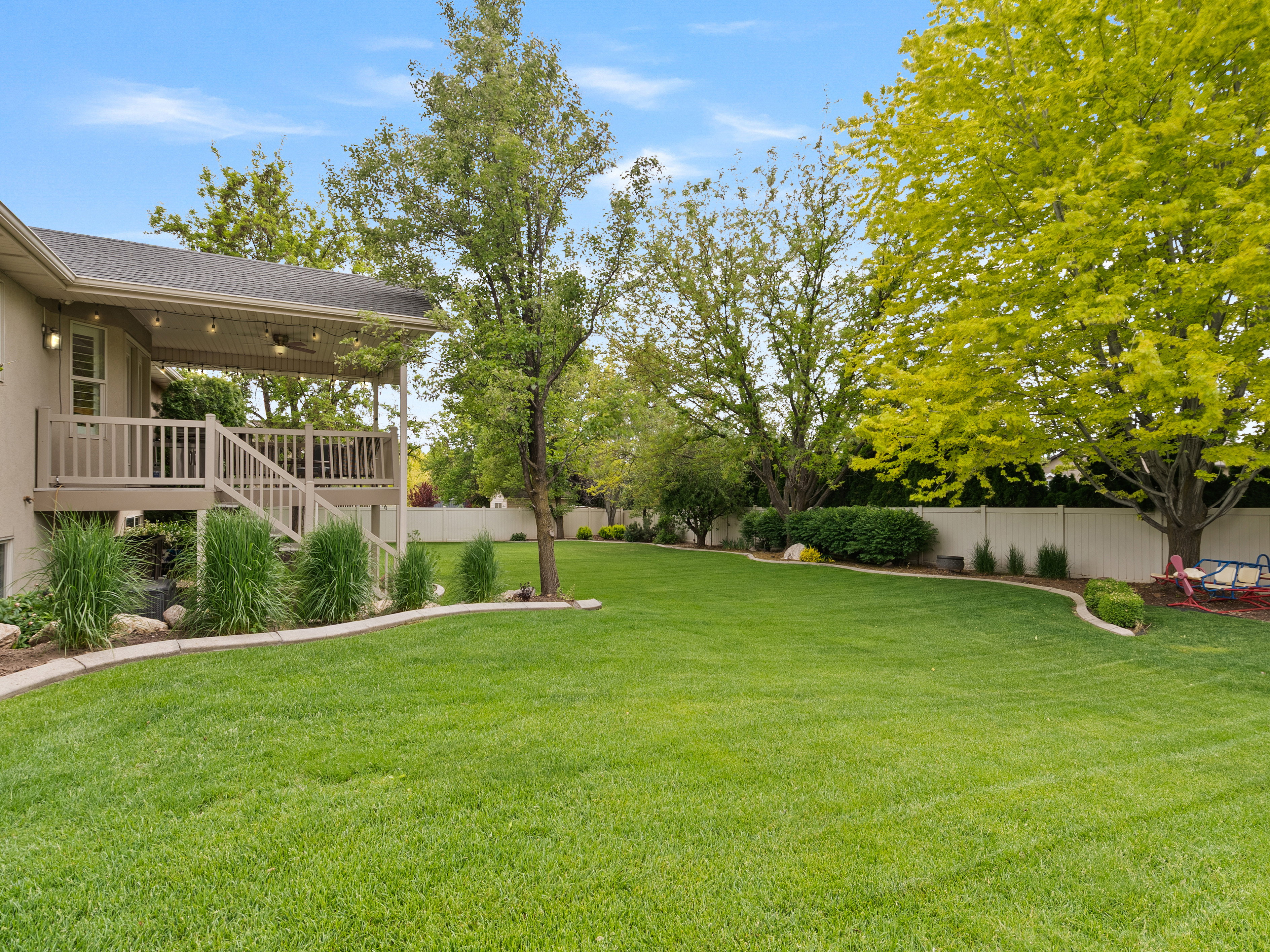 Expansive backyard featuring a manicured lawn, established perimeter landscaping, mature trees, and a privacy fence