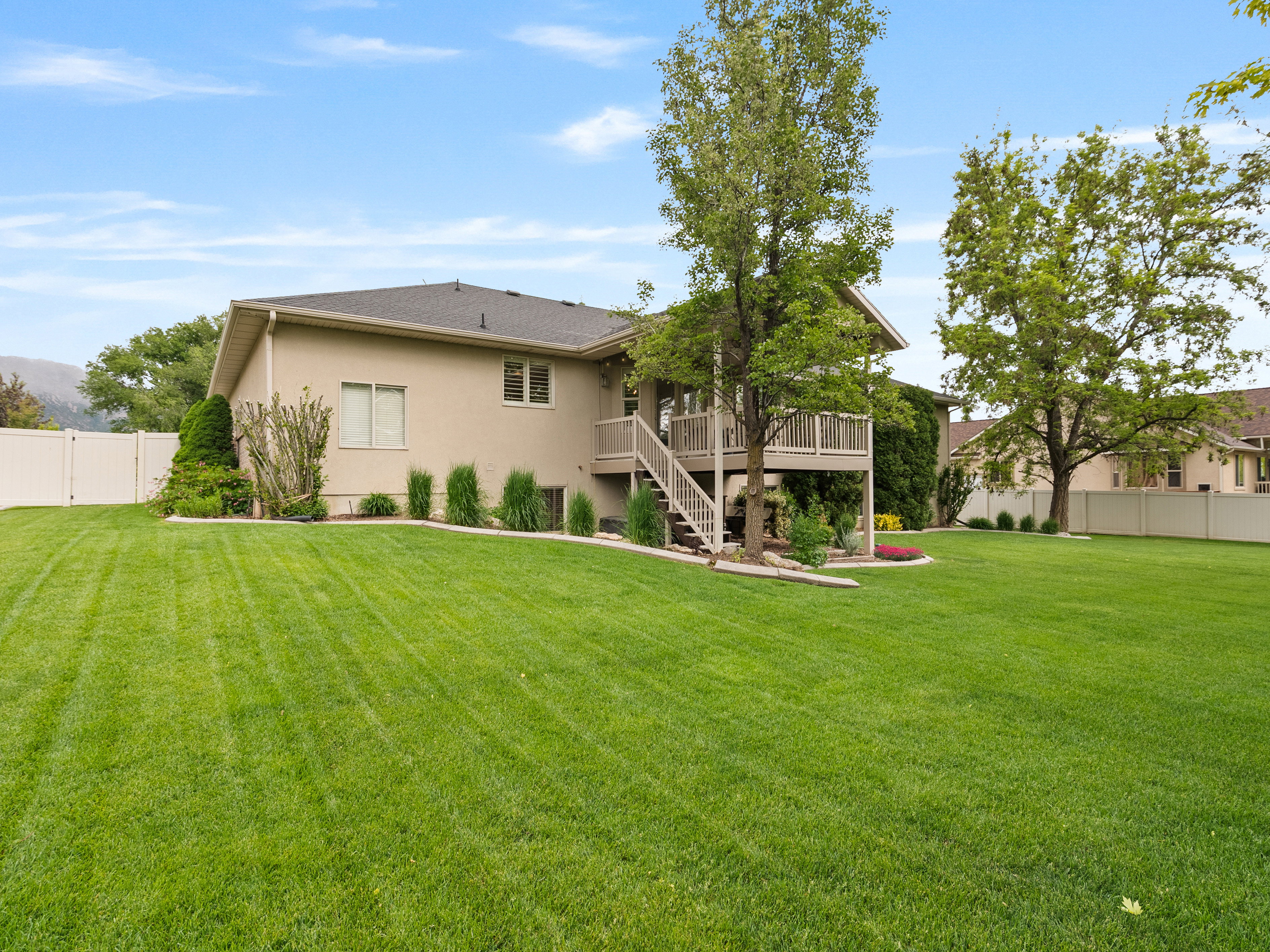 Expansive rear lawn featuring a two-story deck with staircase access, mature trees, and perimeter fencing