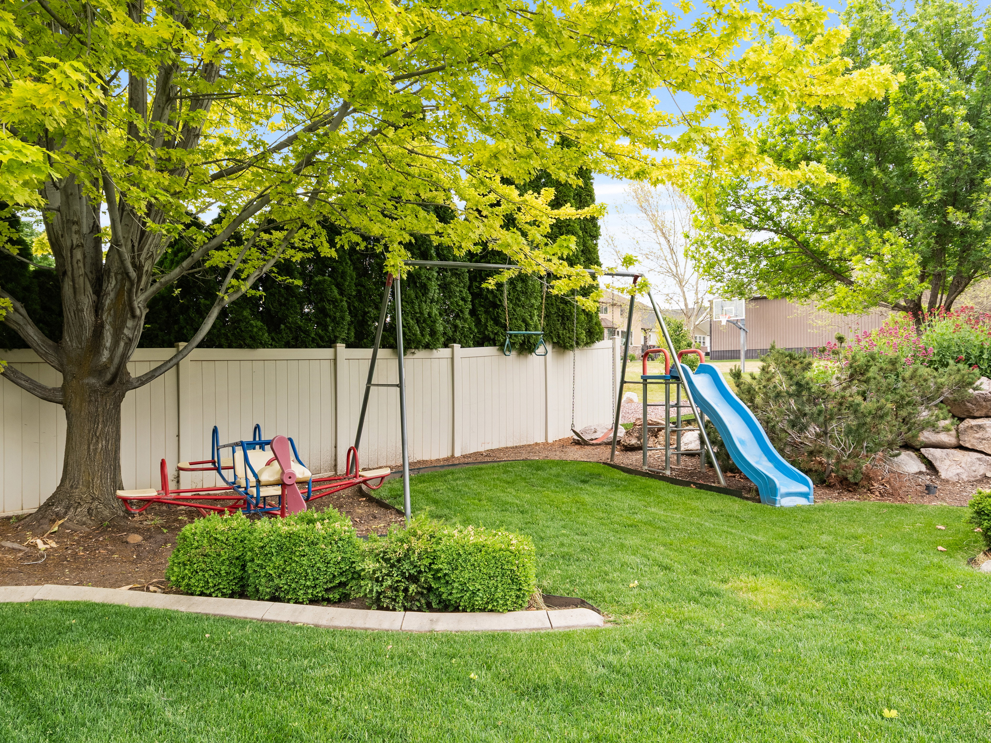 Expansive backyard featuring a lush lawn, mature trees providing natural shade, and a white privacy fence
