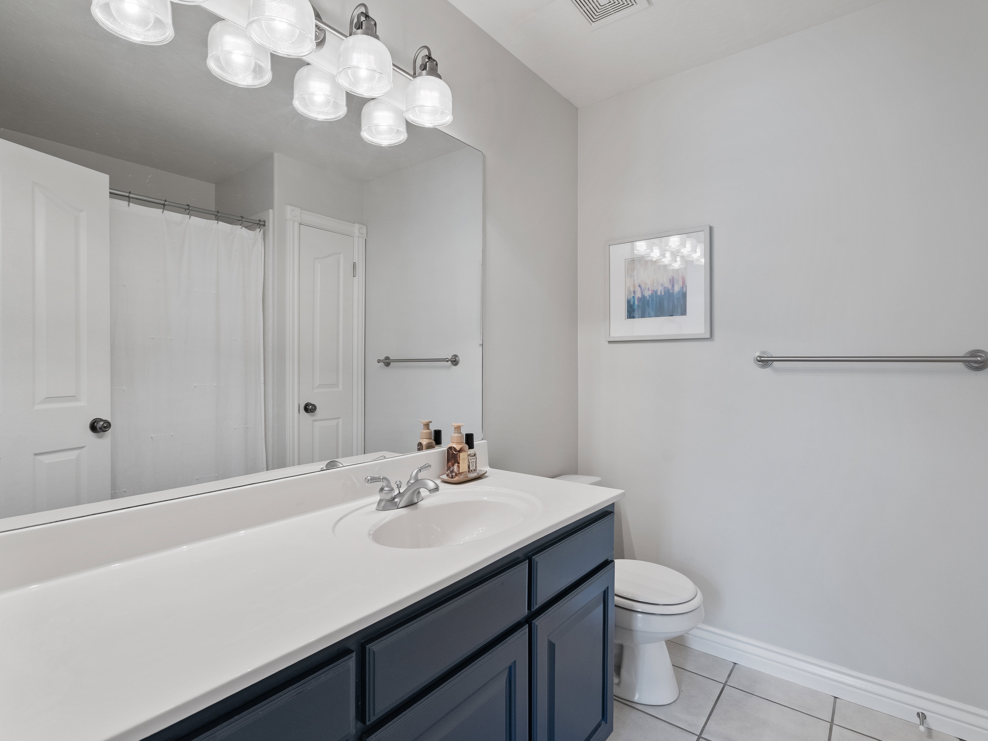 Bathroom featuring a single vanity with a white countertop and blue cabinetry, a toilet, a full-width mirror, and a multi-bulb vanity light fixture