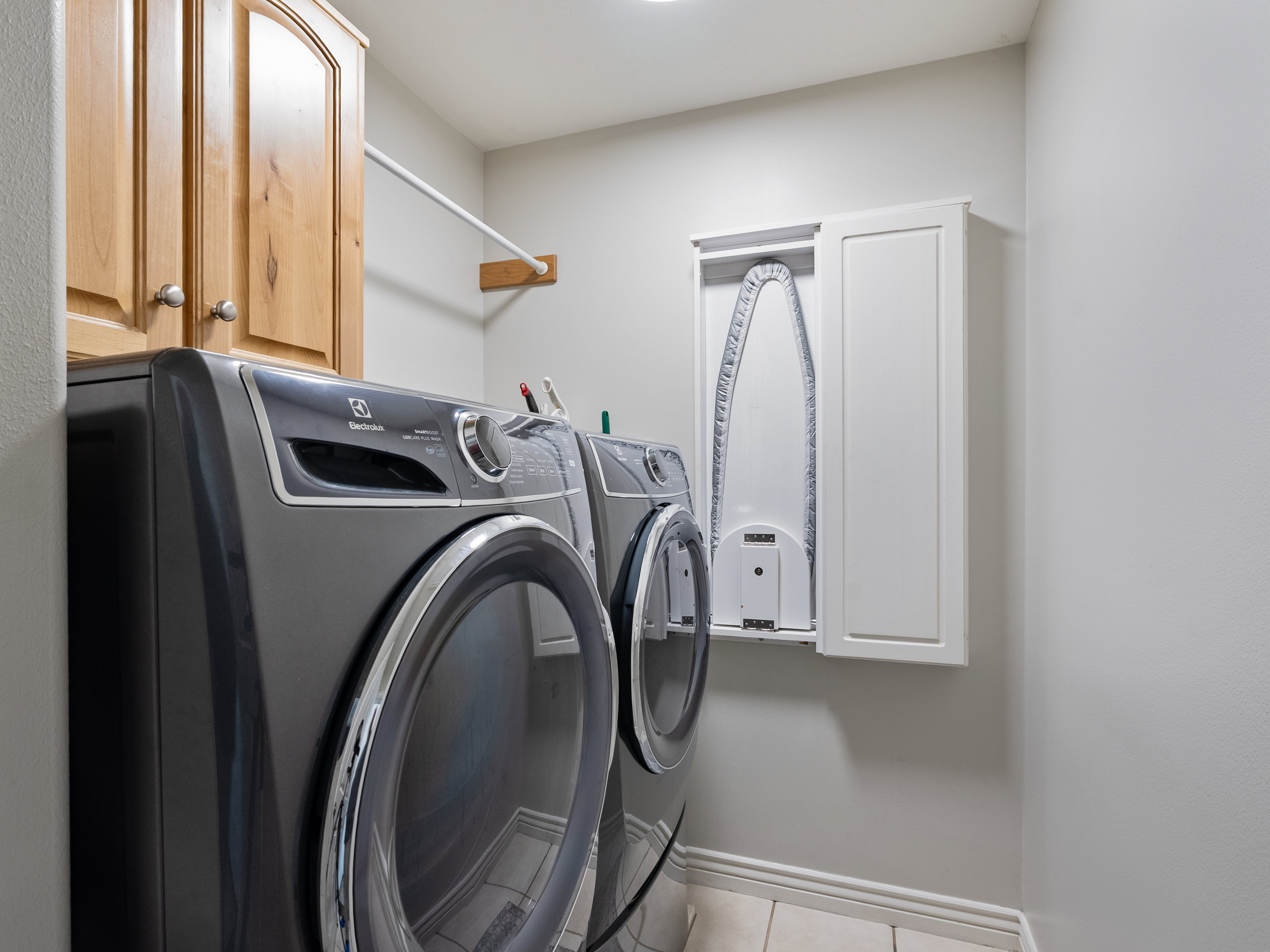 Dedicated laundry area featuring light wood cabinetry, a wall-mounted drying rod, and a built-in folding ironing board