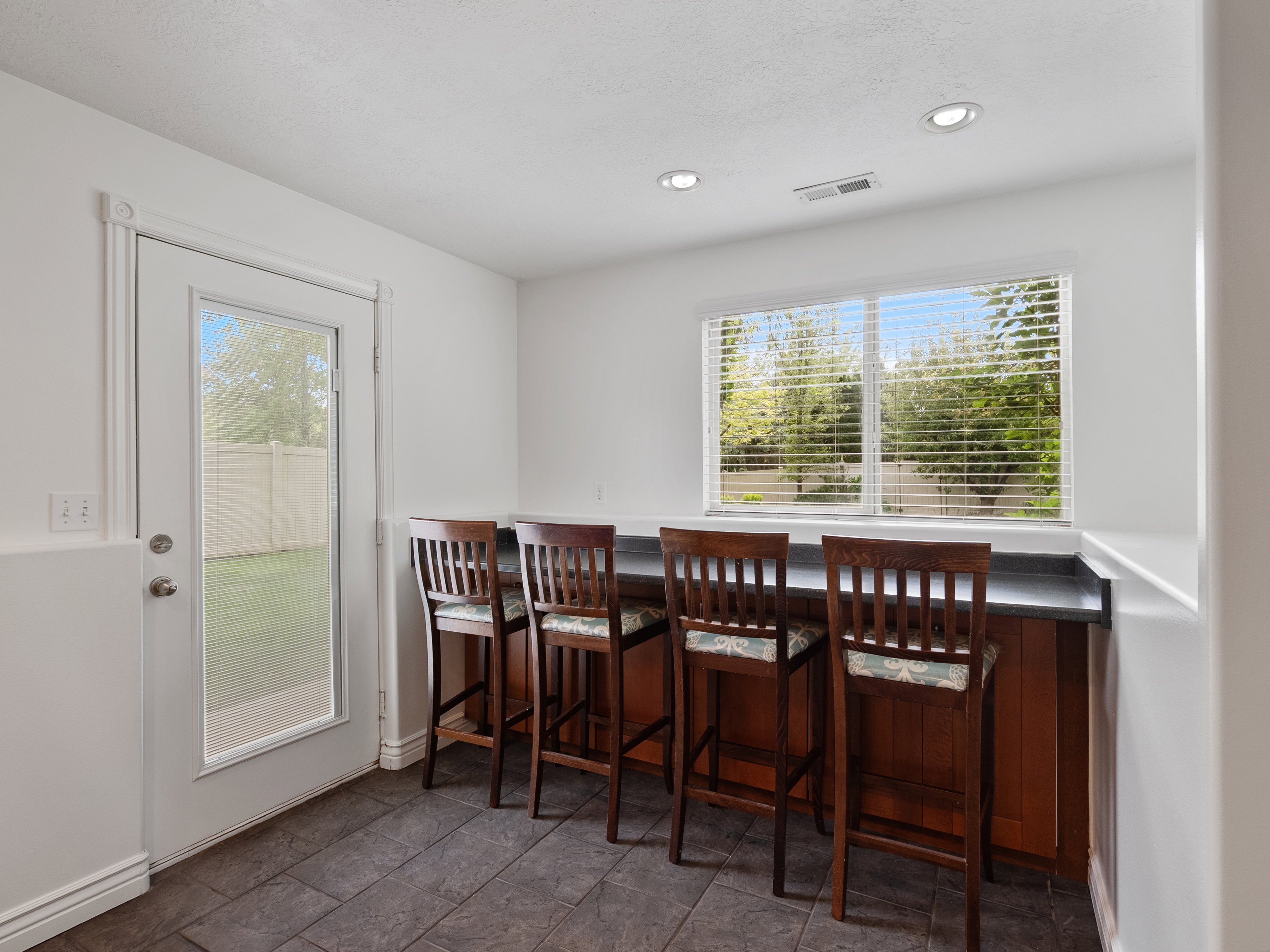 Built-in bar with wood cabinetry, dark countertop, and a window with horizontal blinds