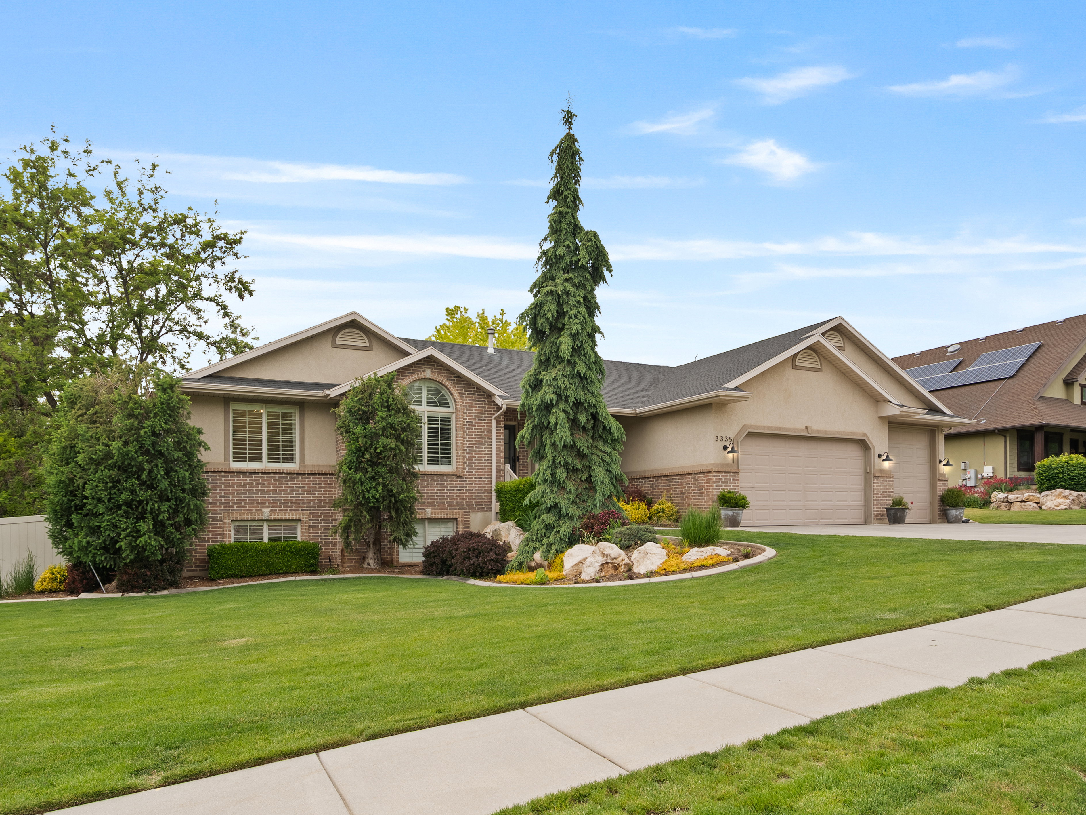 Stucco and brick exterior with arched window detailing, an attached two-car garage, and established landscaping featuring a prominent evergreen