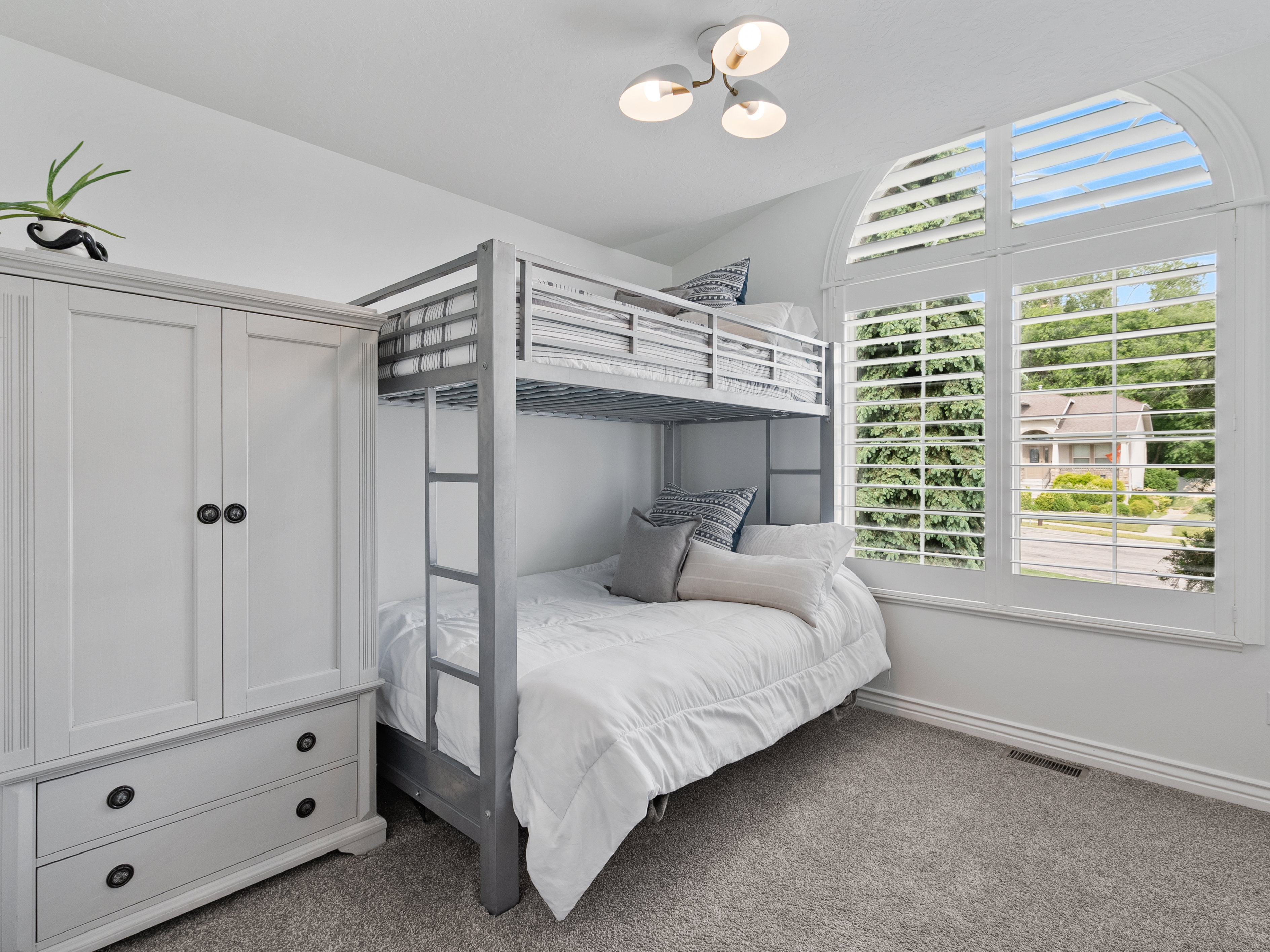 Room featuring a large arched window with white plantation shutters, gray carpet flooring, and a contemporary three-light ceiling fixture