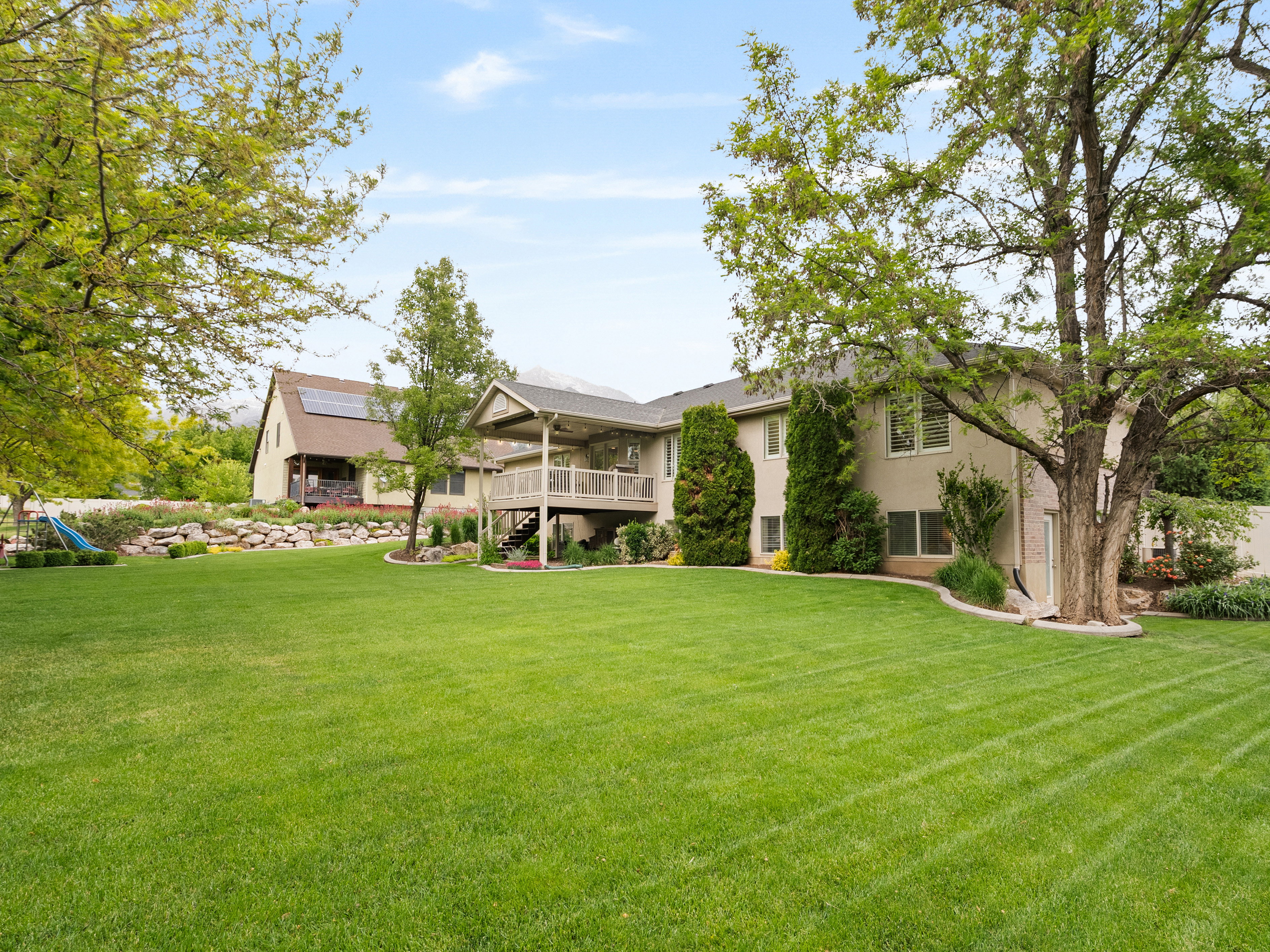 Expansive backyard featuring a manicured lawn, mature trees, and a multi-level deck with a covered portion