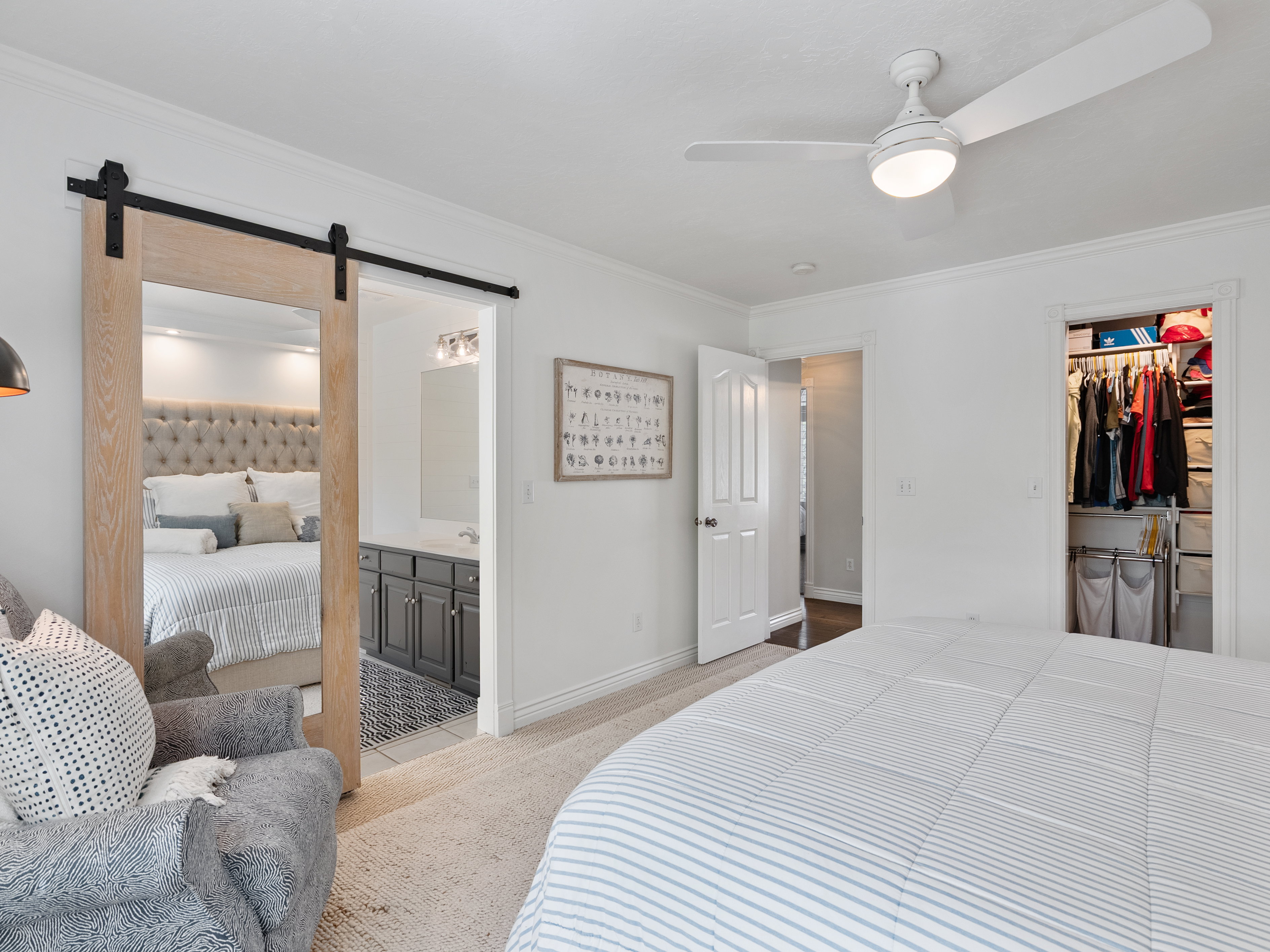 Bedroom featuring a barn door entry to a bathroom with a dual vanity, a ceiling fan with integrated lighting, an open closet with shelving, and light-toned carpet flooring