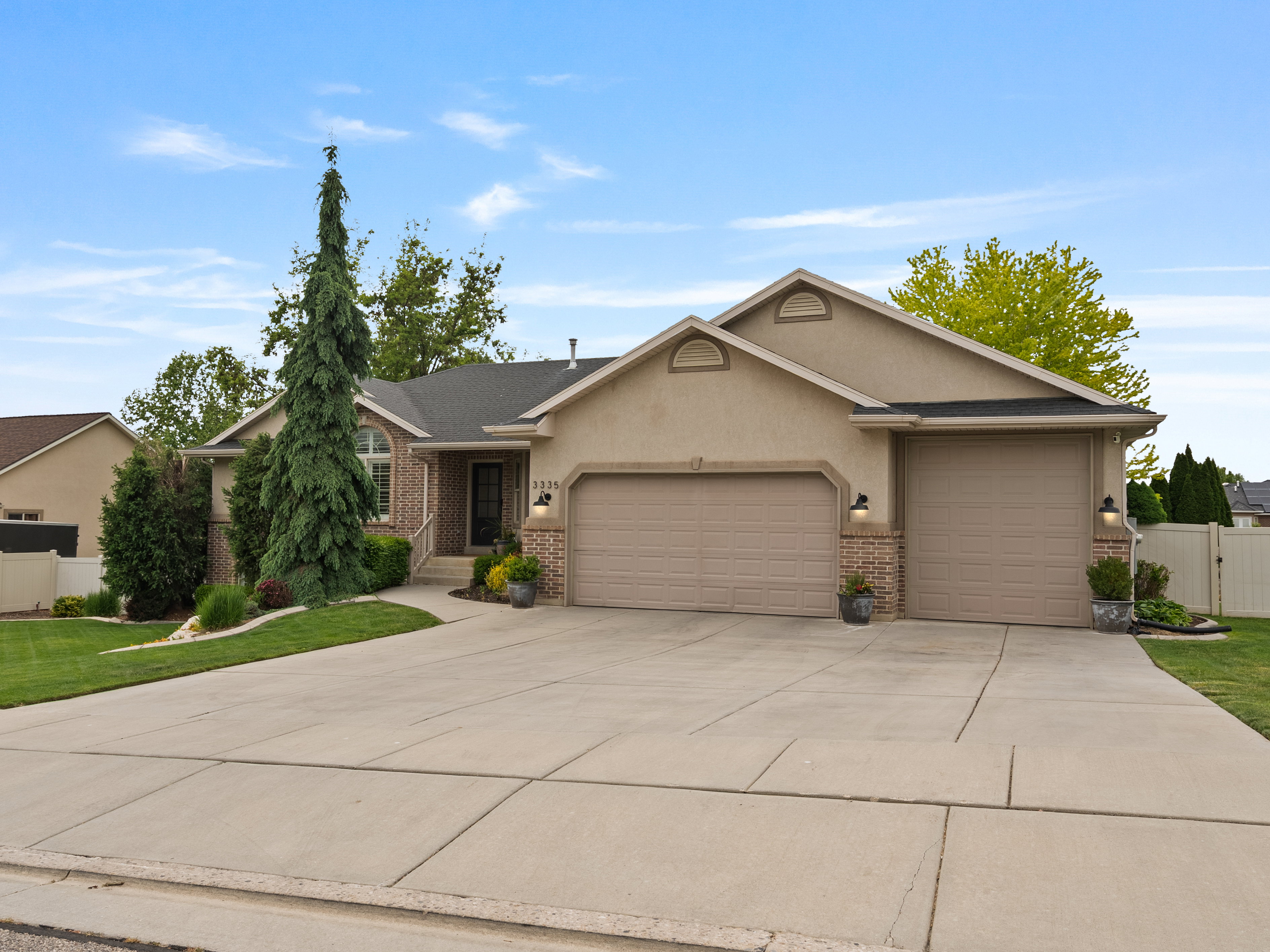 Stucco exterior with brick accents, featuring two attached garages, a concrete driveway, and manicured landscaping