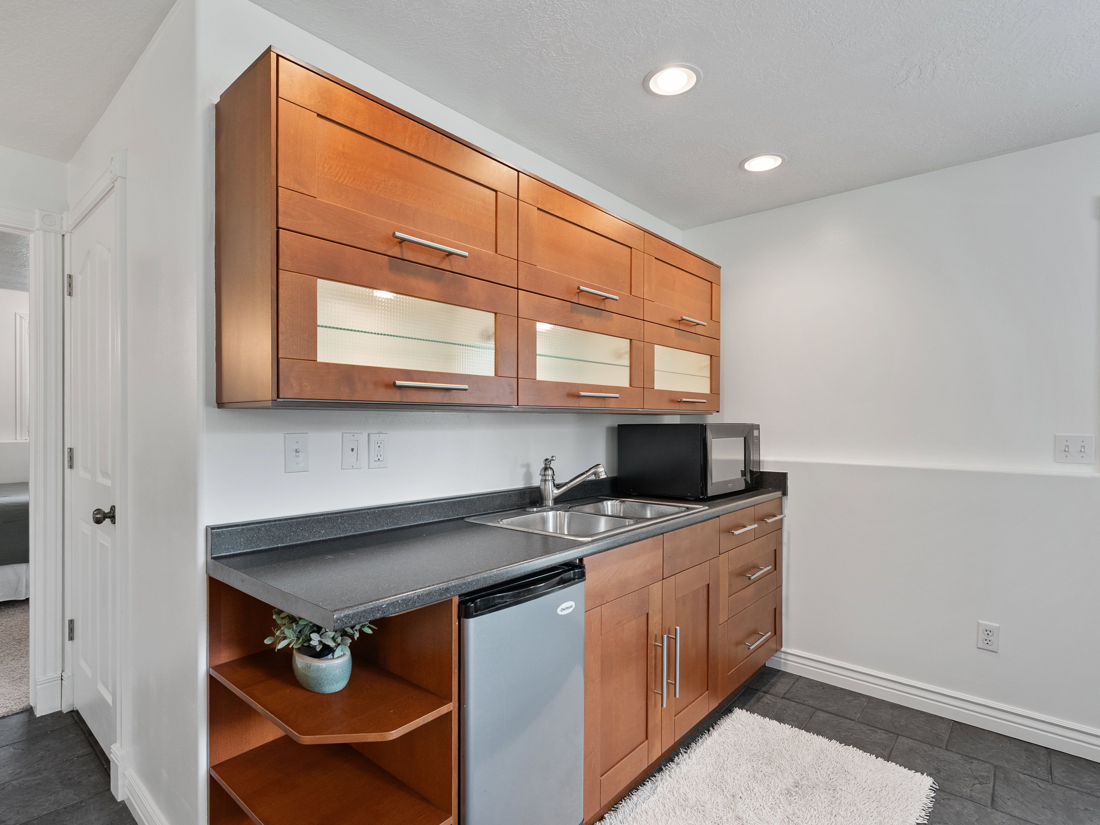 Compact wet bar featuring cherry wood-finish cabinetry, a dual basin stainless steel sink, and dark stone-finish countertops