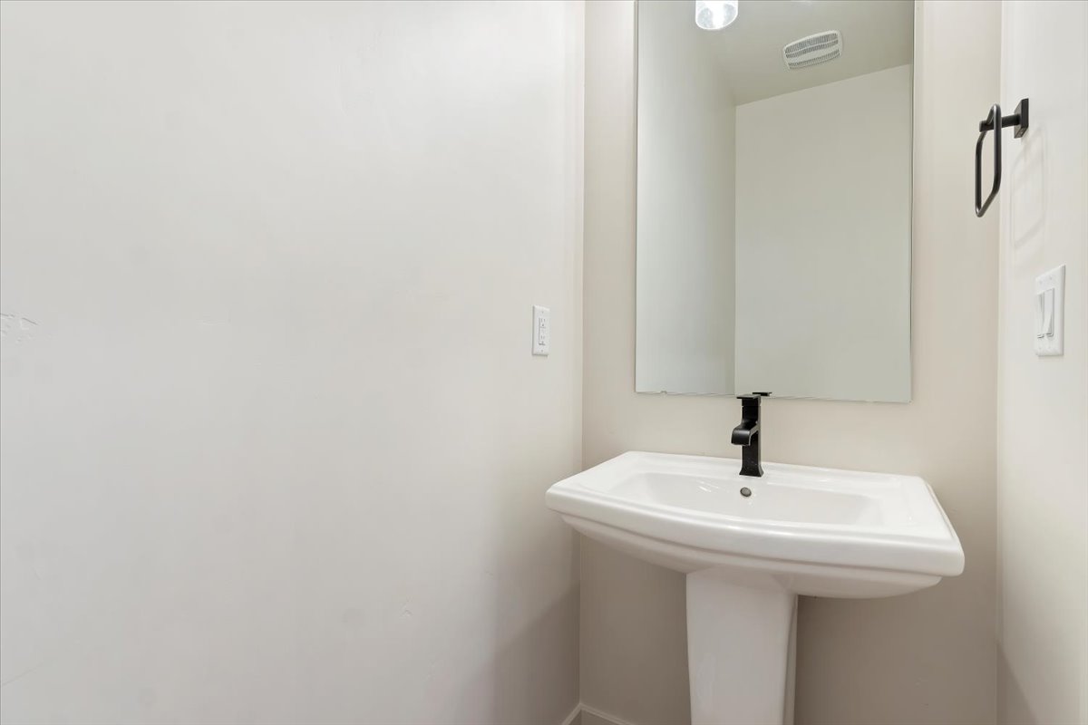 White pedestal sink with a contemporary black faucet, framed by a rectangular mirror
