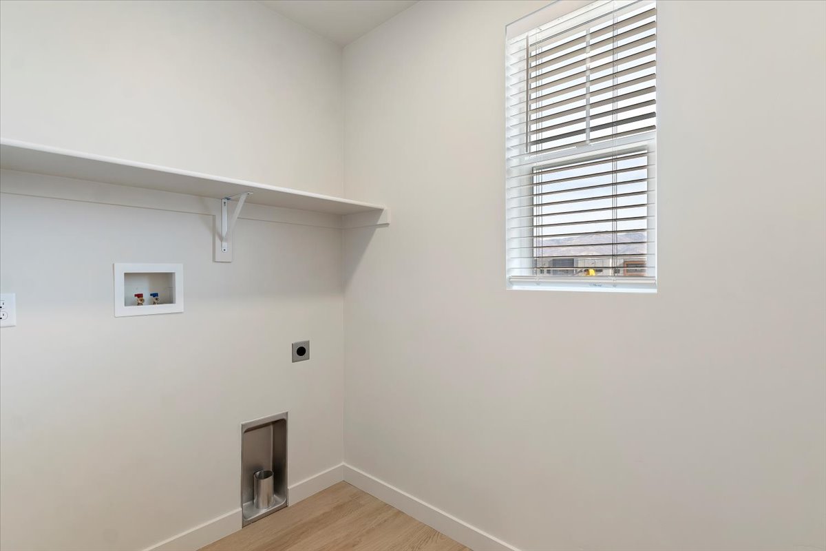 Dedicated laundry area featuring a window with blinds, wall-mounted shelving, and wood-finish flooring