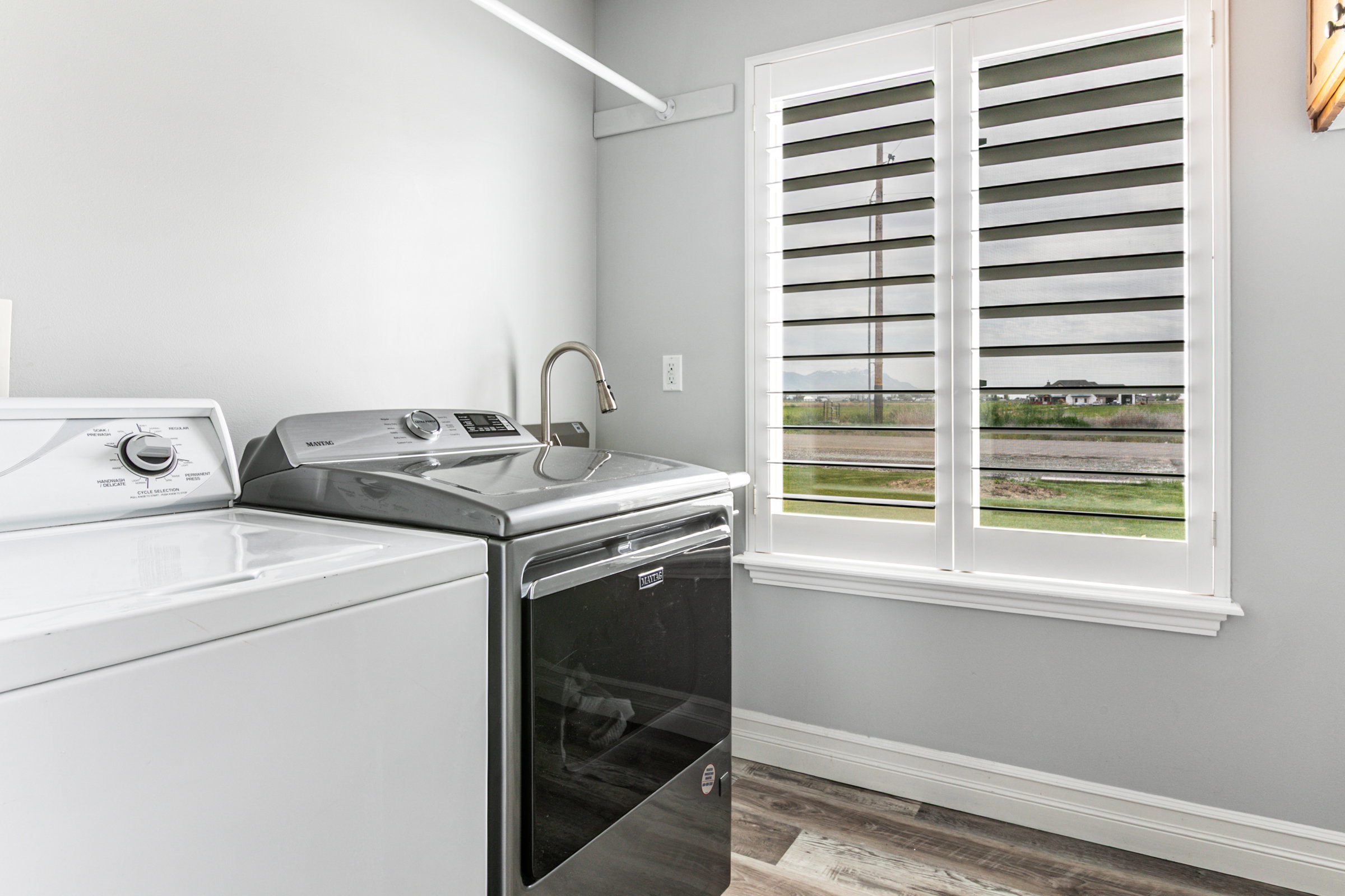 Laundry area featuring wood-finish flooring, a utility sink with a gooseneck faucet, and a double window with plantation shutters