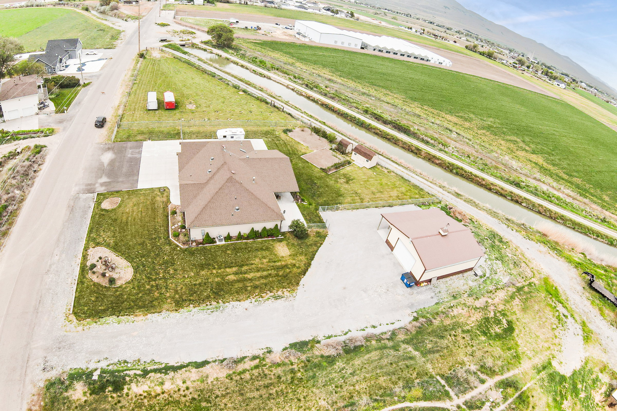 Expansive lot featuring a single-story residence with a brown shingle roof, a detached metal-sided outbuilding with a brown roof, a concrete driveway, and established landscaping