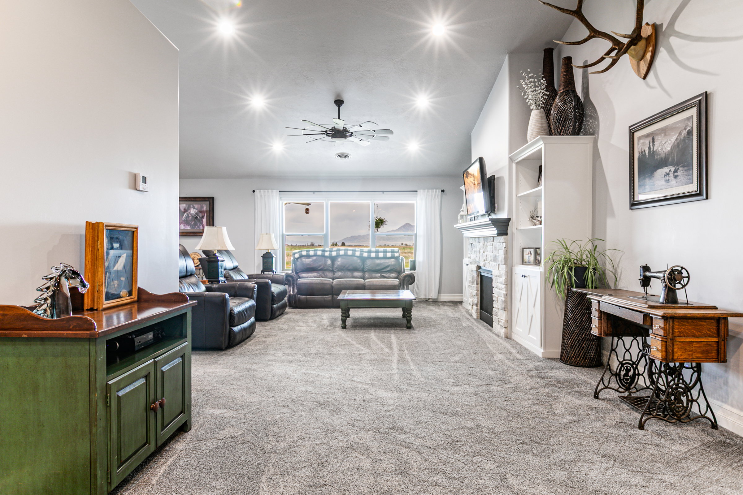 Spacious living area featuring neutral carpeting, a stone-clad fireplace with built-in shelving, vaulted ceilings with recessed lighting, and a contemporary ceiling fan