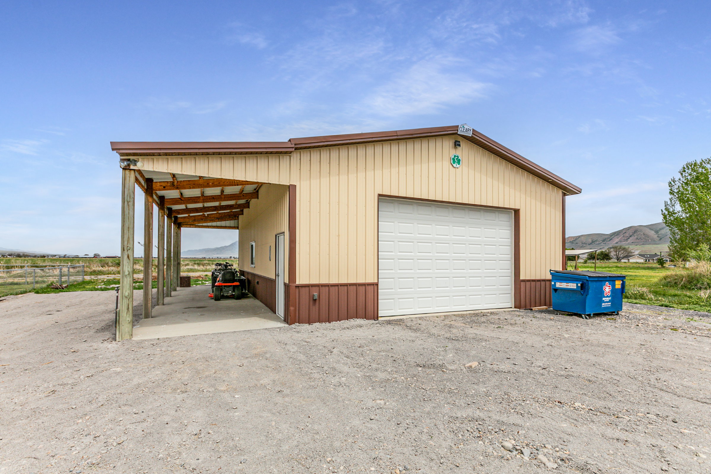 Metal-sided outbuilding featuring a large white garage door, attached carport with a concrete pad, and a pedestrian entry door