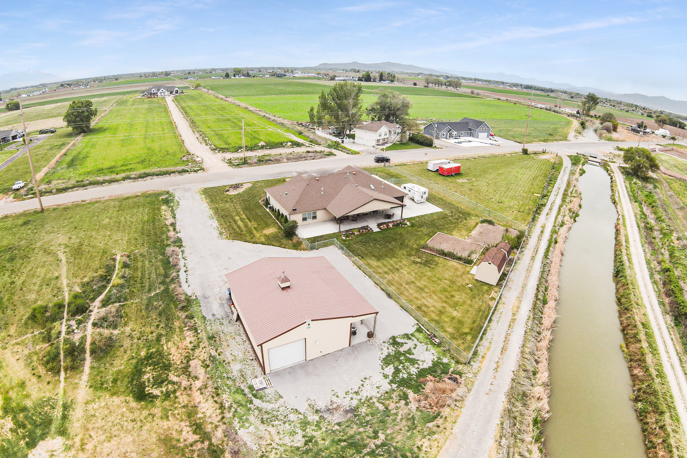 Expansive rural property featuring a large detached garage with multiple bays, a single-story residence with a covered patio, and a separate storage shed