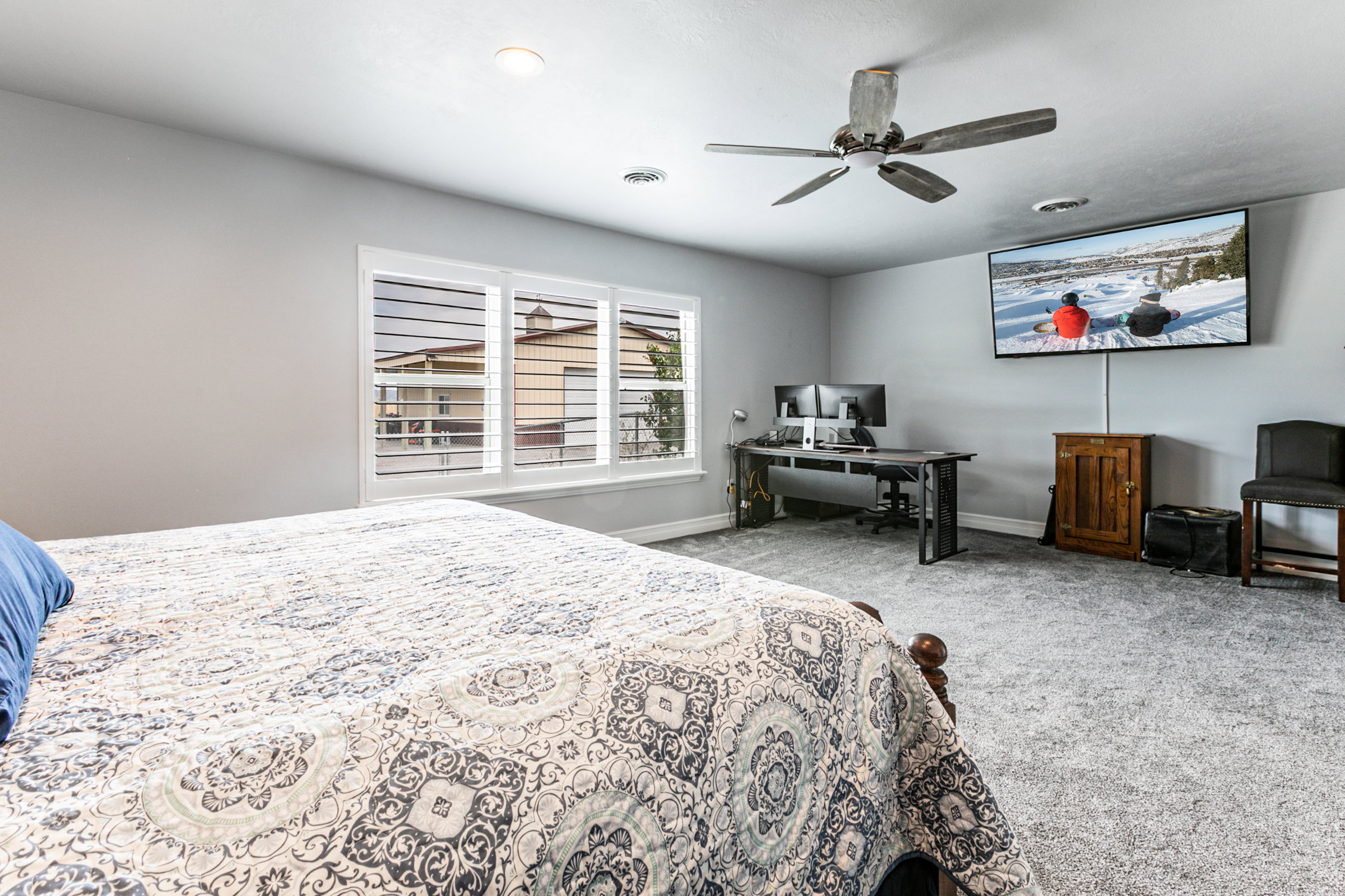 Spacious room featuring light gray walls, plush gray carpet, a multi-panel window with white horizontal blinds, and a ceiling fan with light fixture