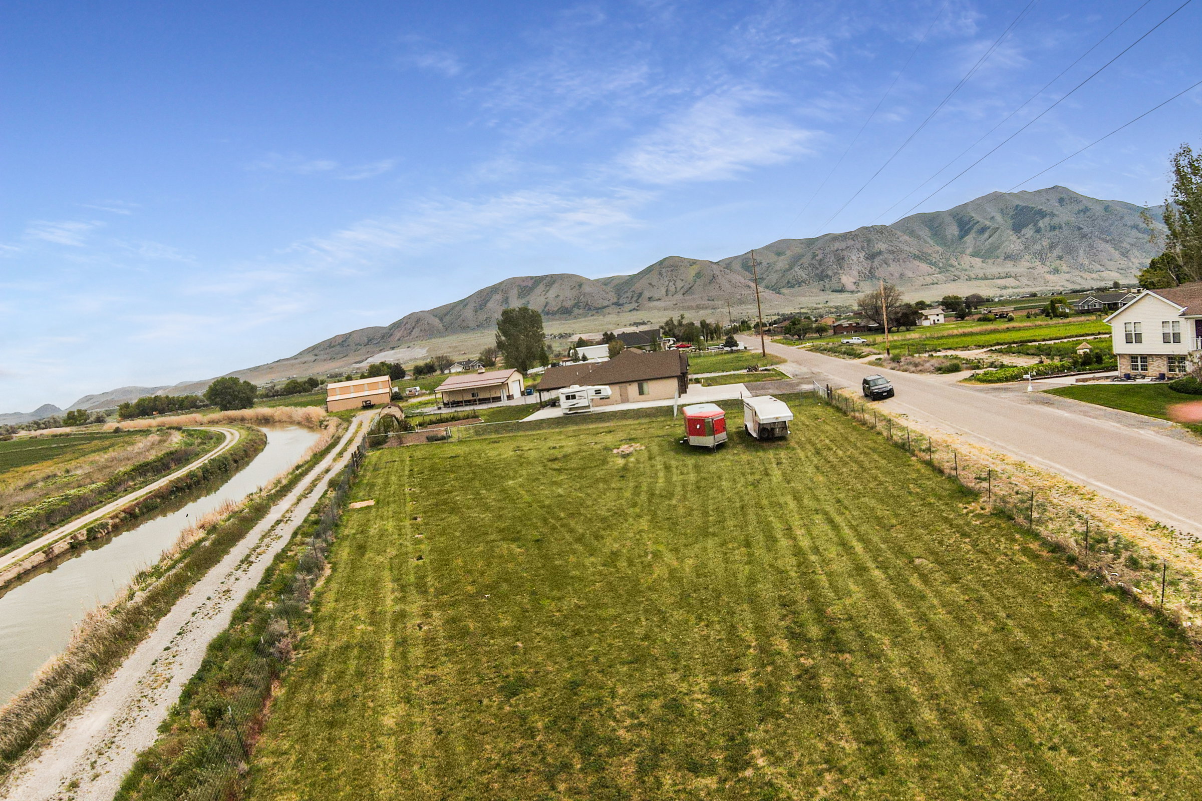 Expansive green space featuring mountain scenery, a paved road, and a concrete-lined canal