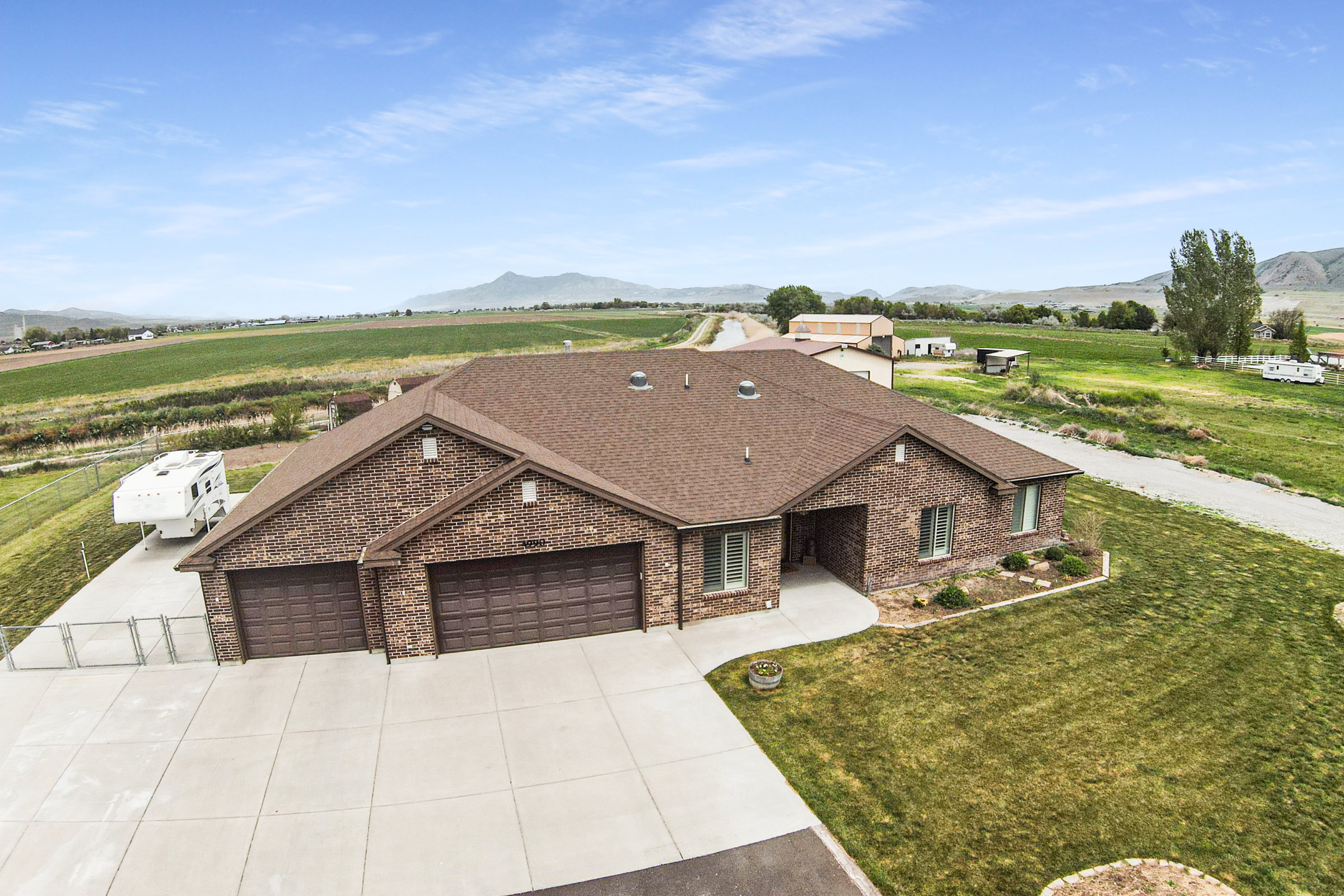 Brick exterior with a multi-car garage, concrete driveway, and surrounding green landscape