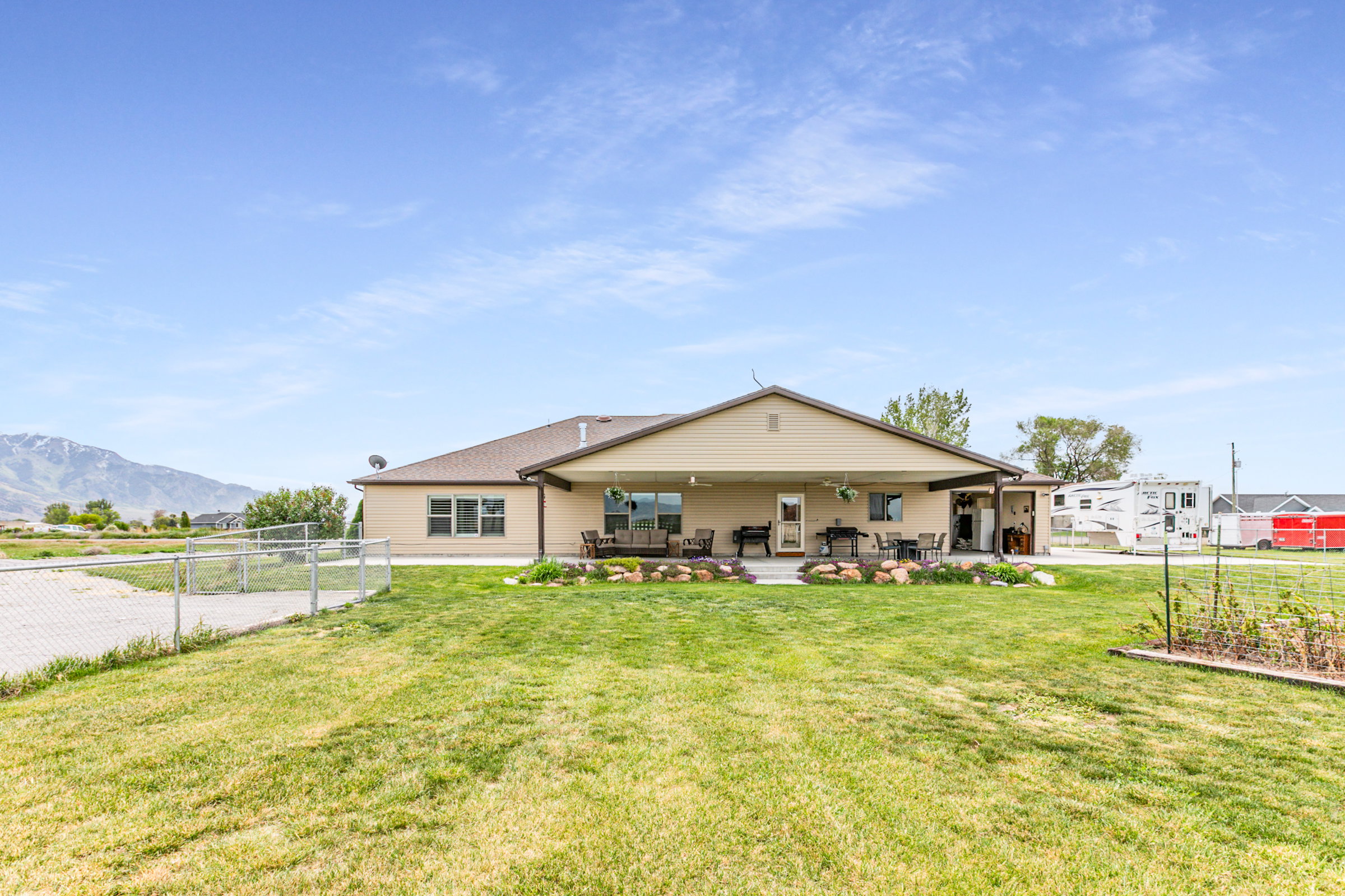 Expansive backyard featuring a covered patio, landscaped rock garden, and a chain-link fence enclosing a gravel area