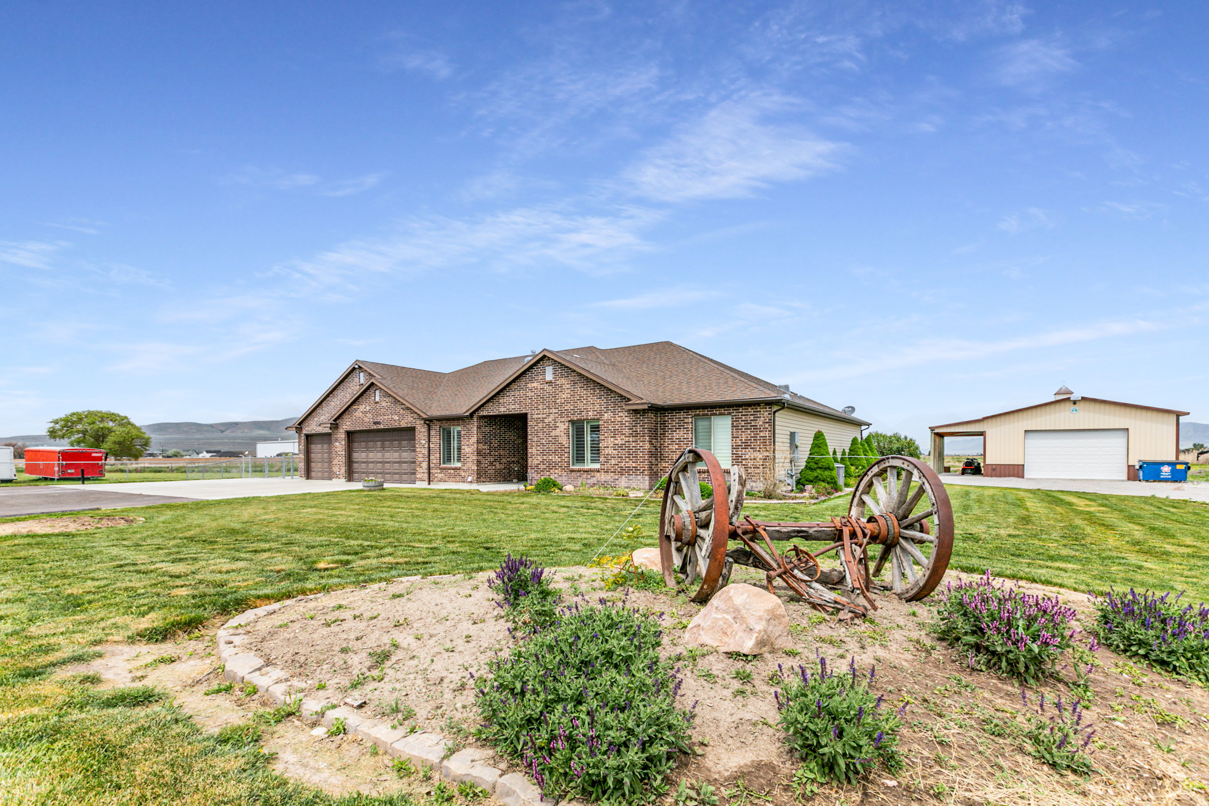 Brick exterior with a multi-car garage, mature landscaping, and a separate outbuilding featuring a roll-up door