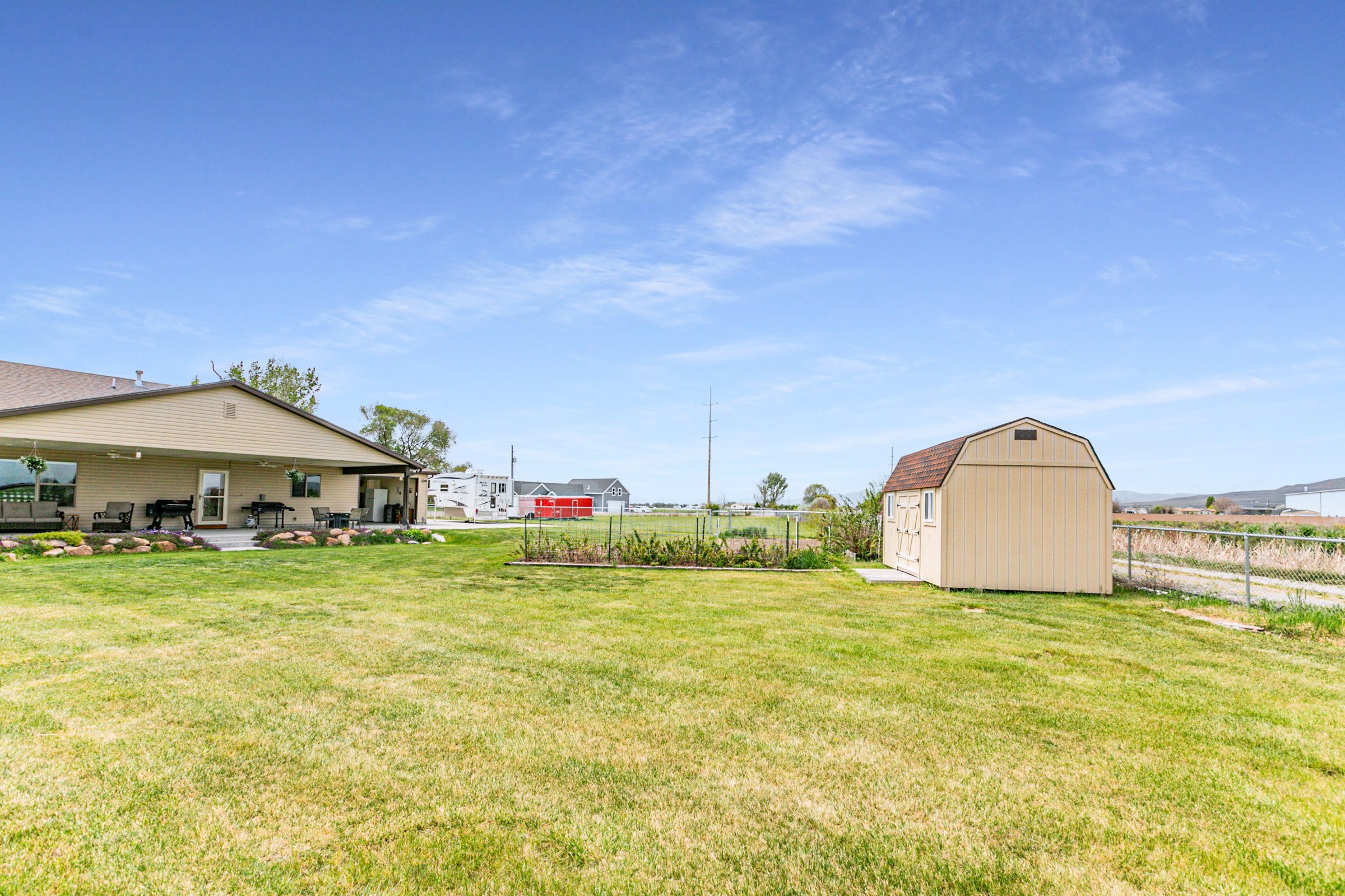 Expansive backyard featuring a covered patio, a separate storage shed, perimeter fencing, and a garden bed