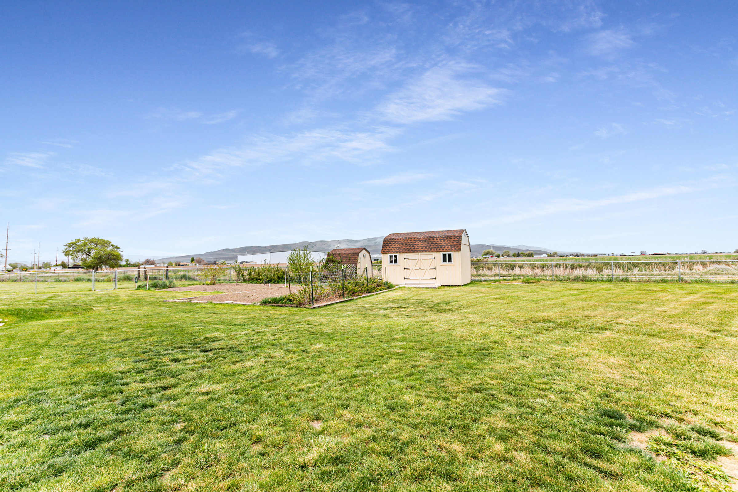 Expansive backyard featuring a manicured lawn, two storage sheds, and a garden bed