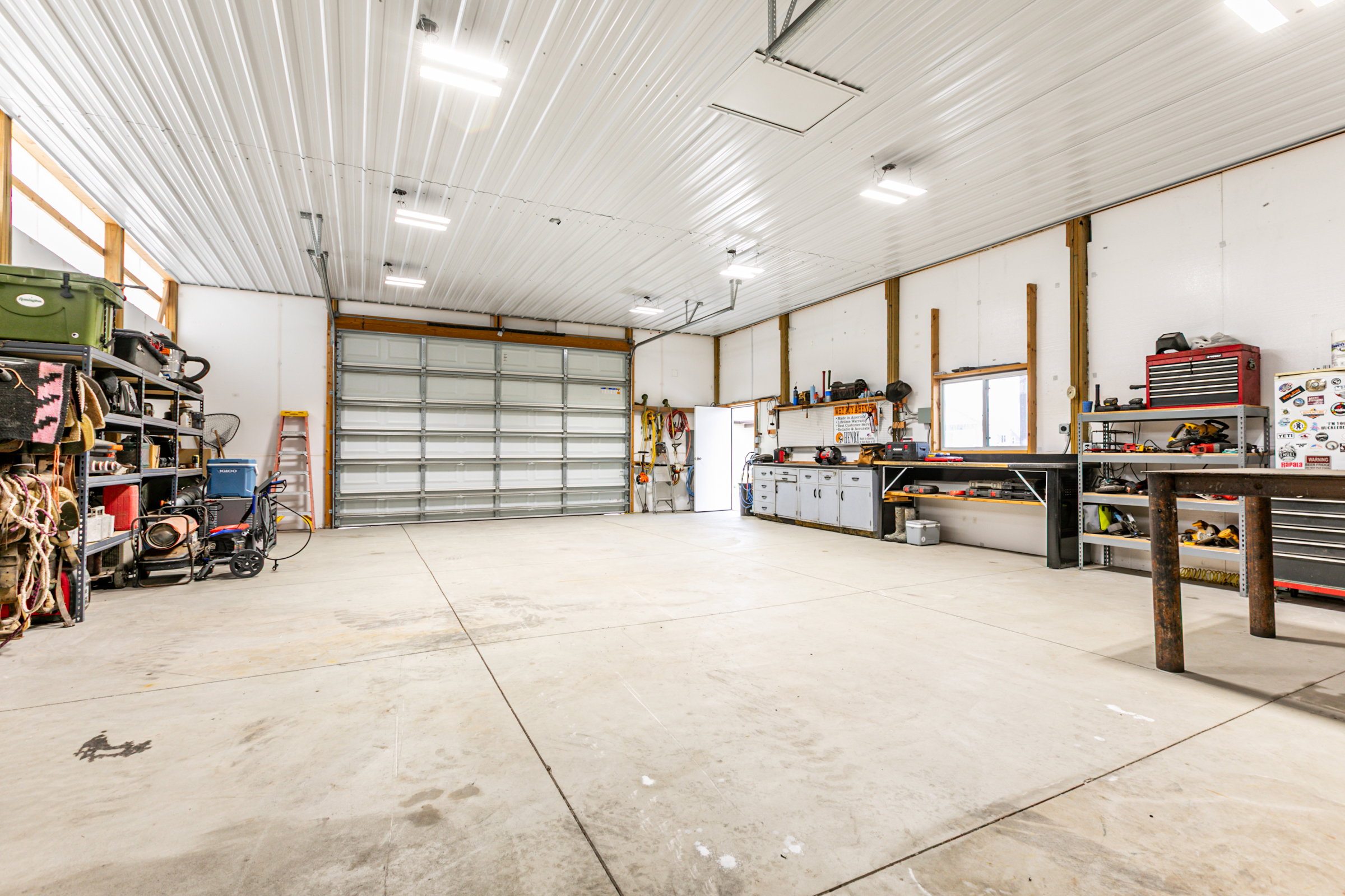 Spacious garage featuring a large roll-up door, concrete flooring, overhead lighting, and built-in workbench cabinetry