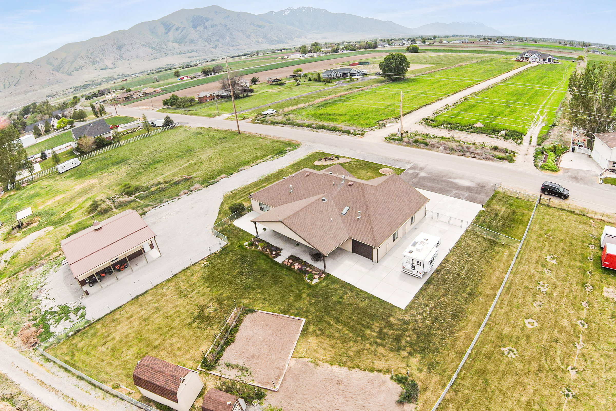 Expansive property featuring a single-story residence with an attached covered patio and garage, a detached carport, and two storage sheds