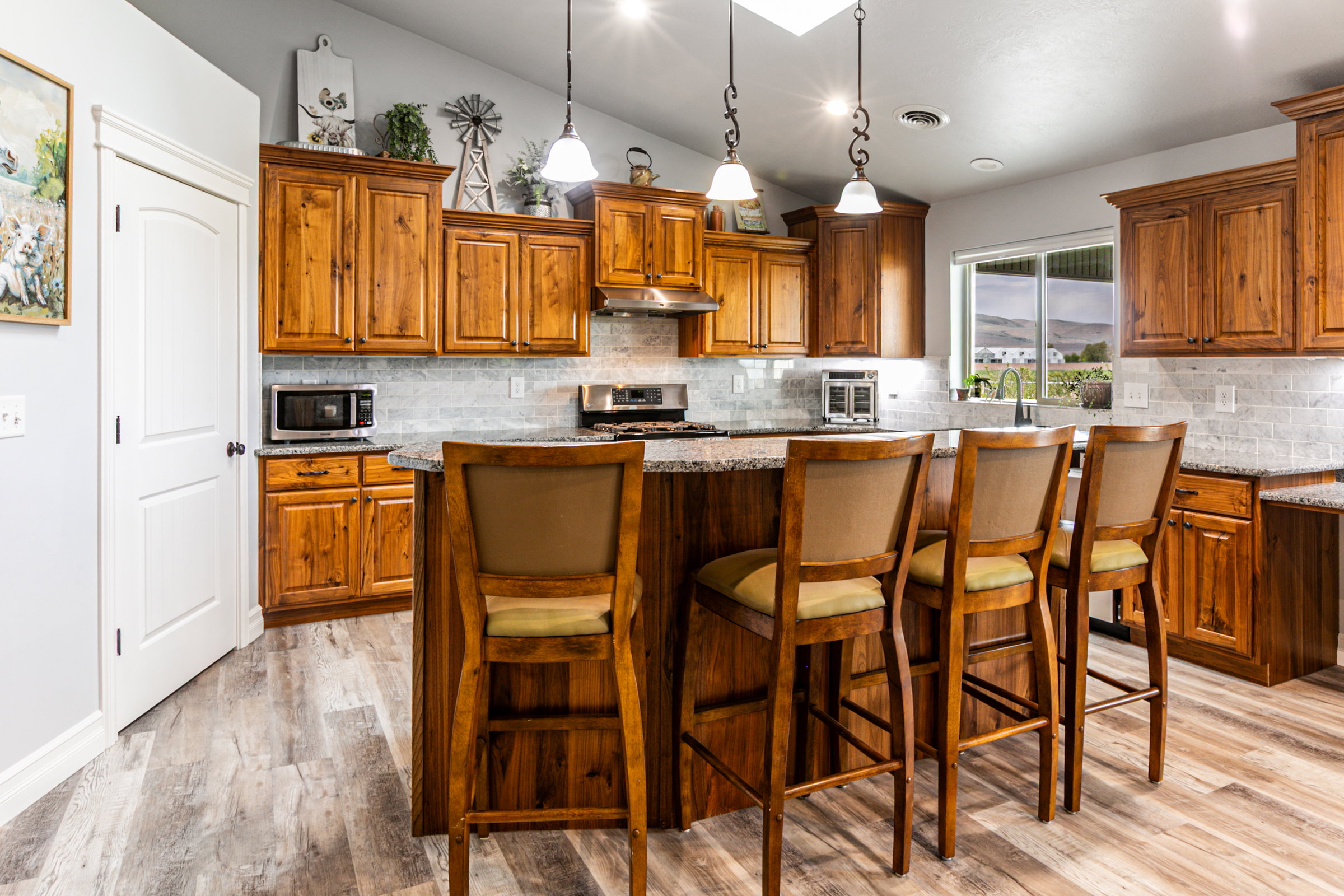 Kitchen featuring wood-finish cabinetry, a central island with countertop seating, stone countertops, a subway tile backsplash, and wood-finish flooring