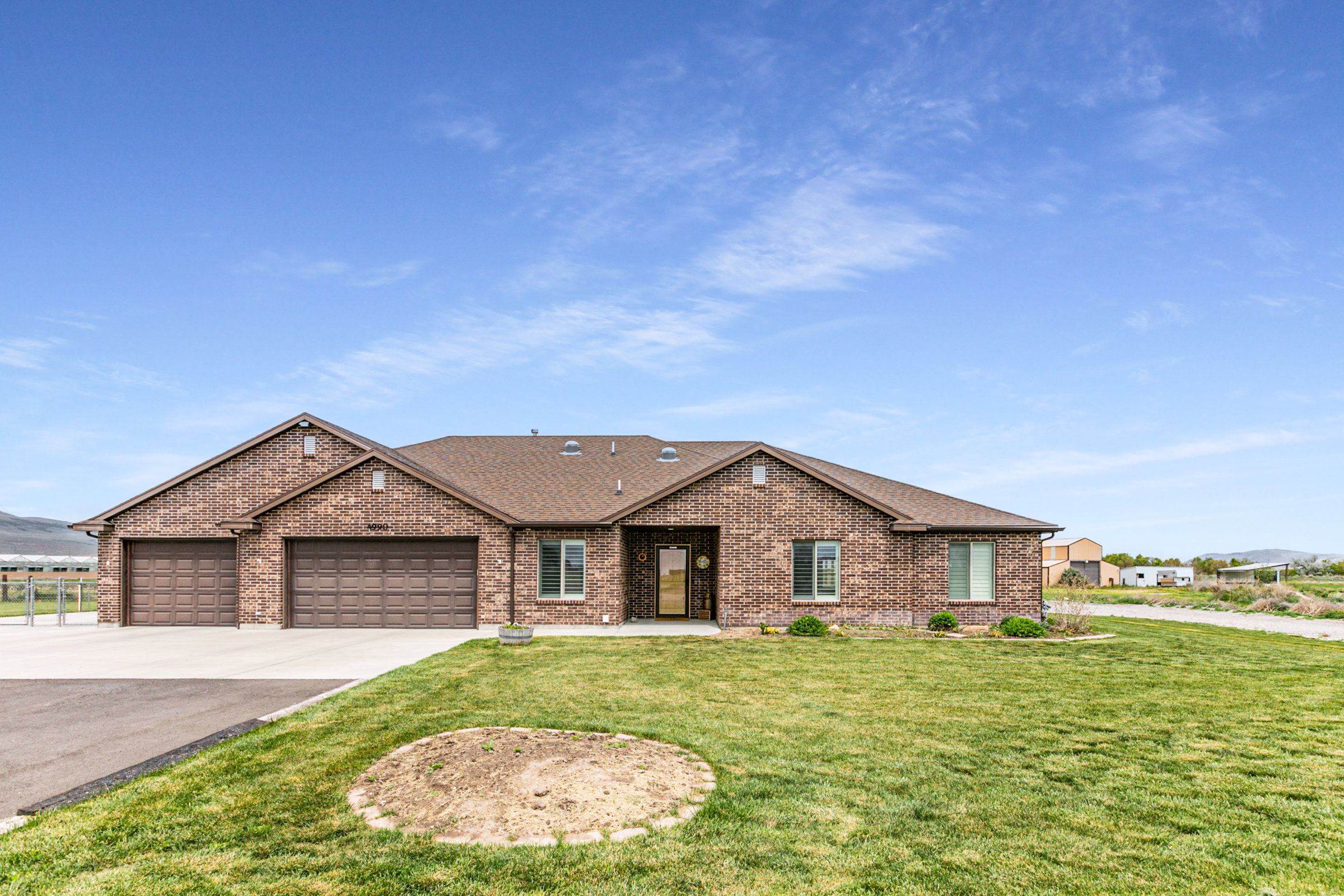 Brick-clad exterior featuring multiple gabled rooflines, an attached three-car garage, front entry with a glass-paneled door, and a spacious green lawn