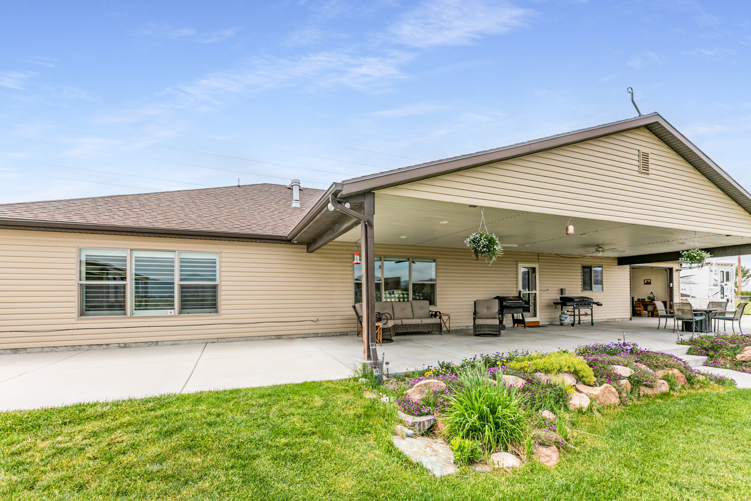 Expansive covered patio featuring a concrete surface, exterior siding, an attached two-car covered parking area, and landscaping with rock accents