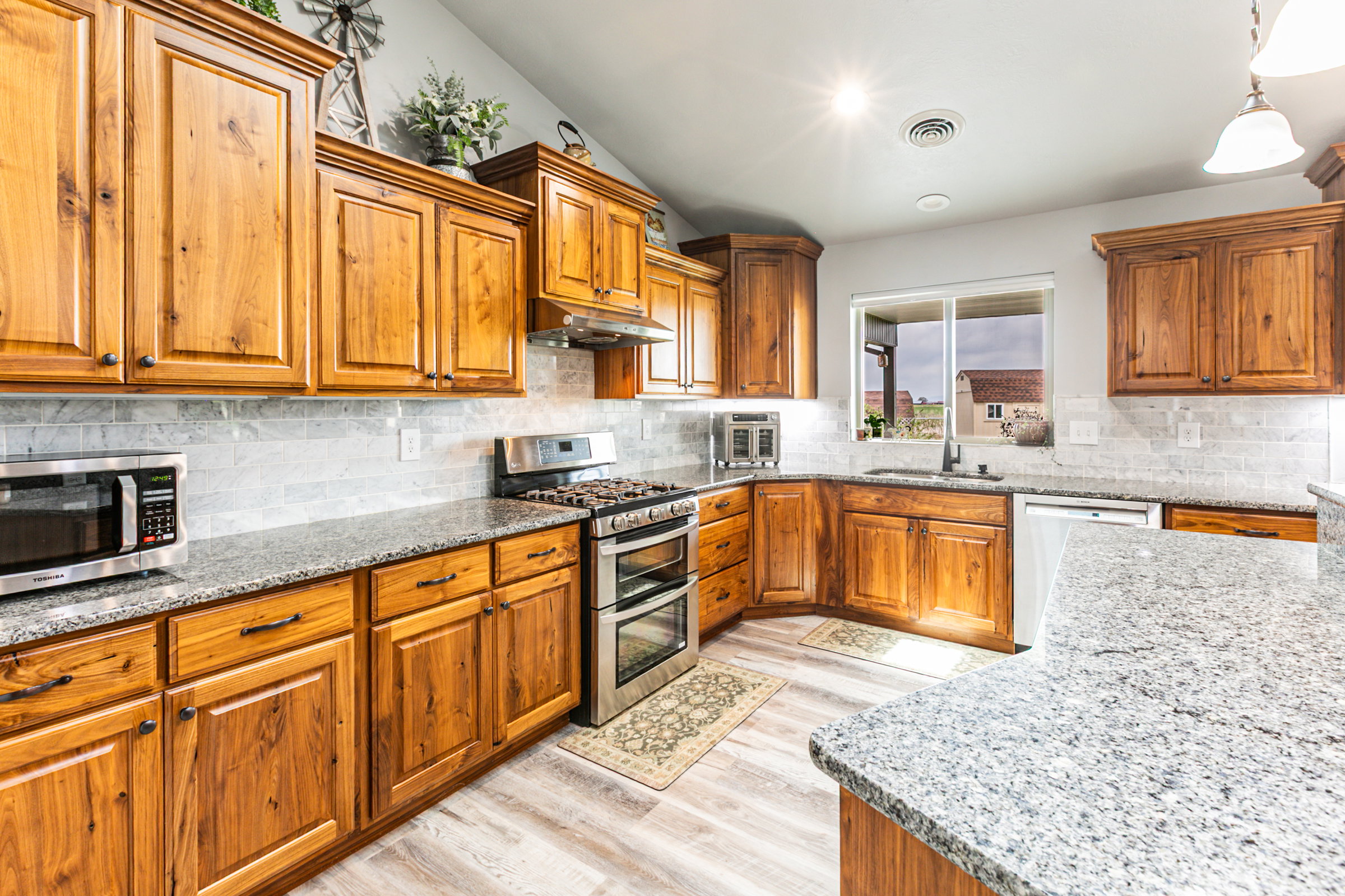 Spacious kitchen featuring extensive wood cabinetry, mottled light-tone countertops, a tile backsplash, stainless steel appliances, and wood-finish flooring
