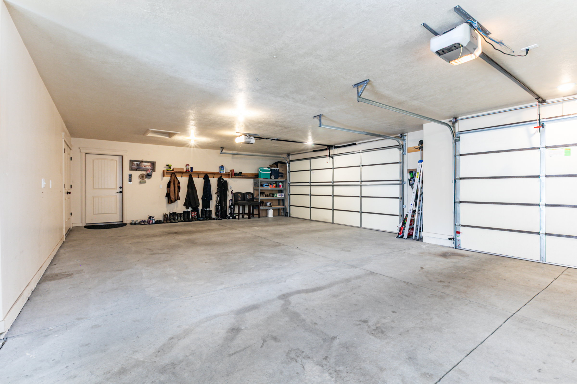 Spacious garage featuring two overhead doors with automatic openers, a pedestrian entry door, concrete flooring, and overhead lighting
