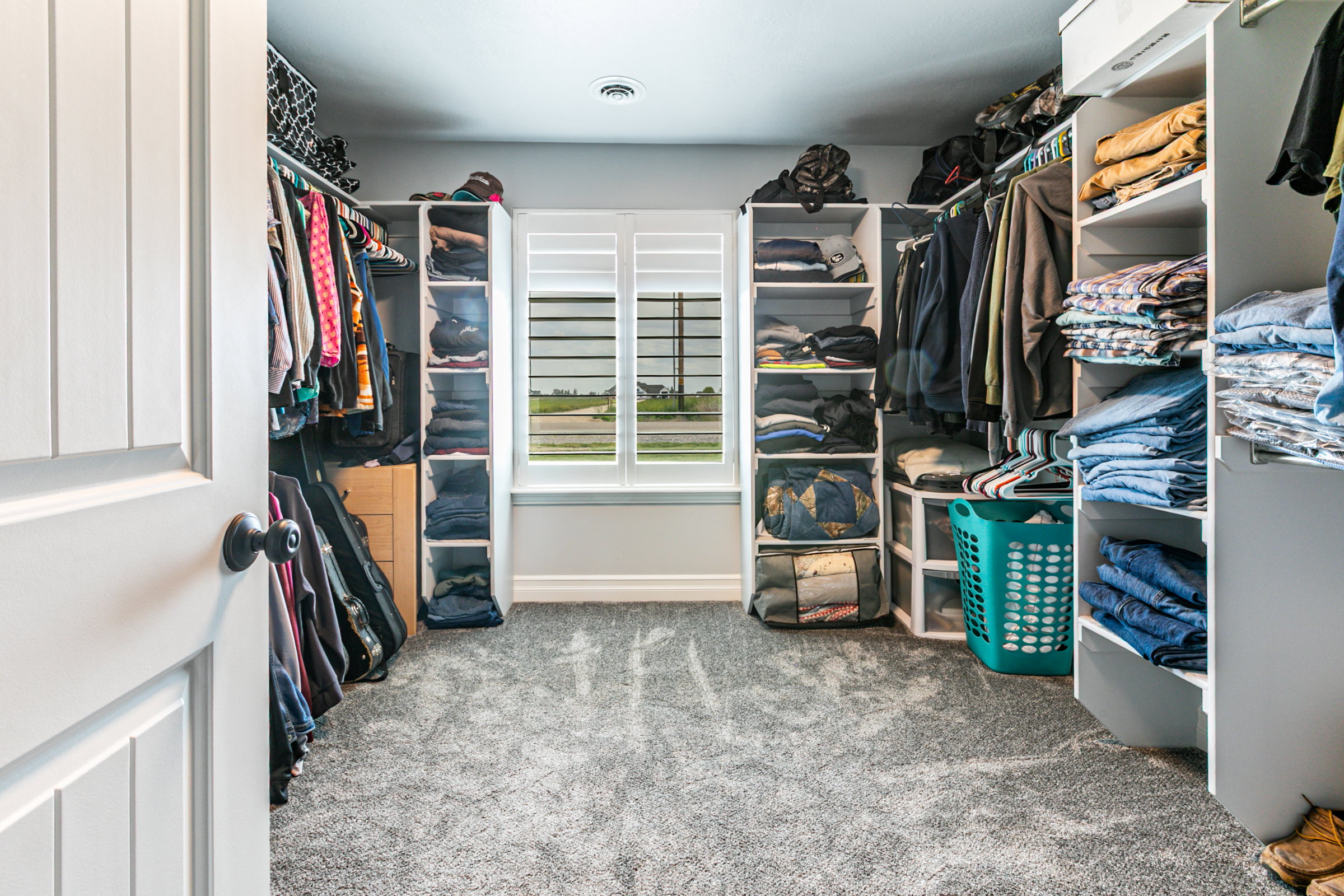 Walk-in closet featuring built-in shelving, hanging rods, grey textured carpet, a window with white louvered shutters, and recessed lighting