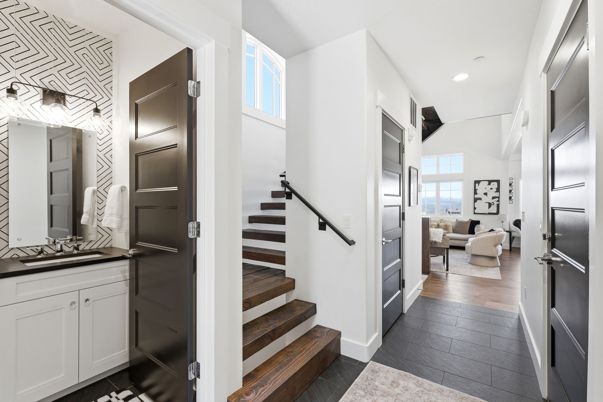 Entryway featuring dark tile flooring, a half-bath with patterned wallpaper and a white vanity, a wood staircase, and dark paneled doors