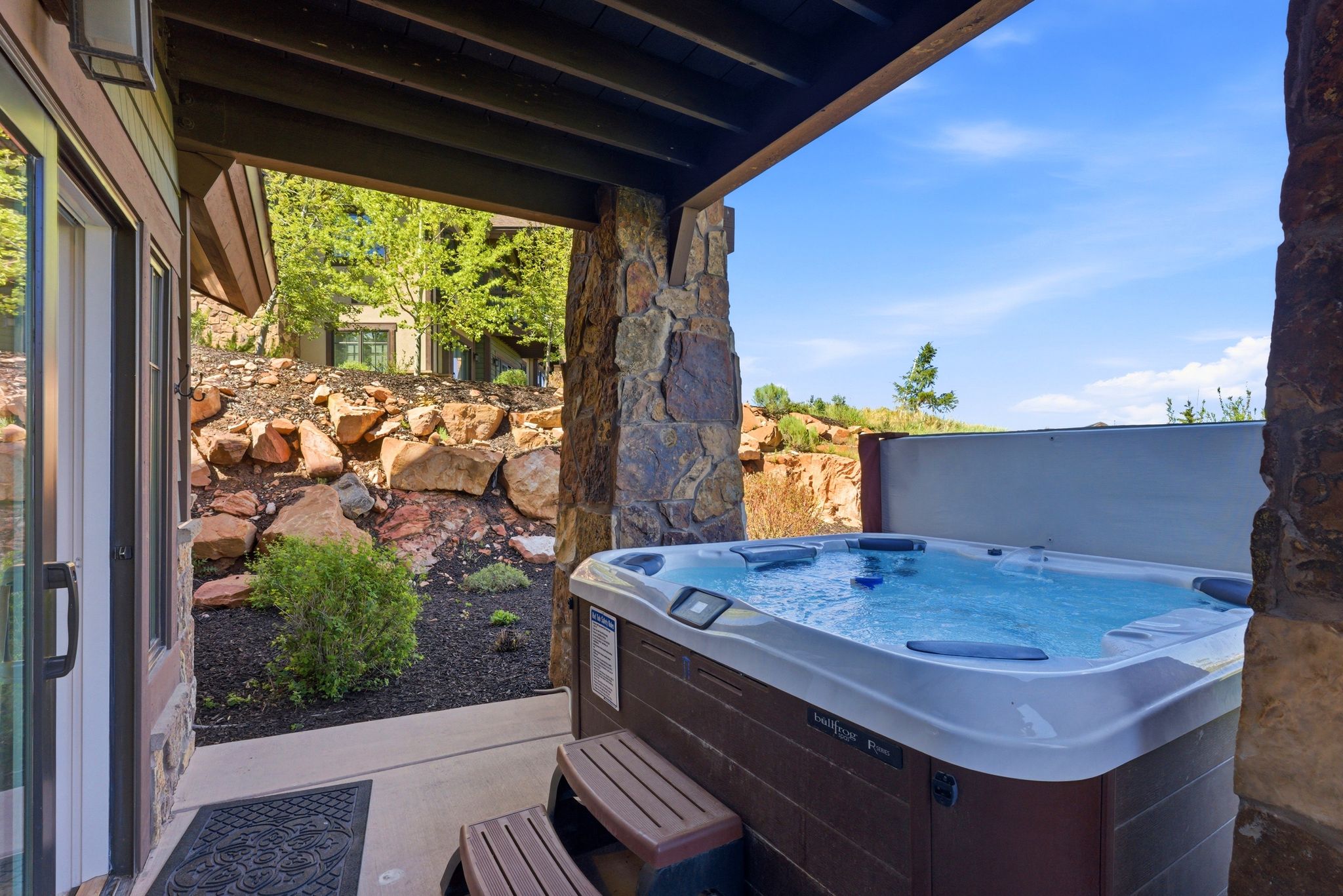 Covered patio featuring a built-in hot tub with steps, stone pillars, and a glass sliding door