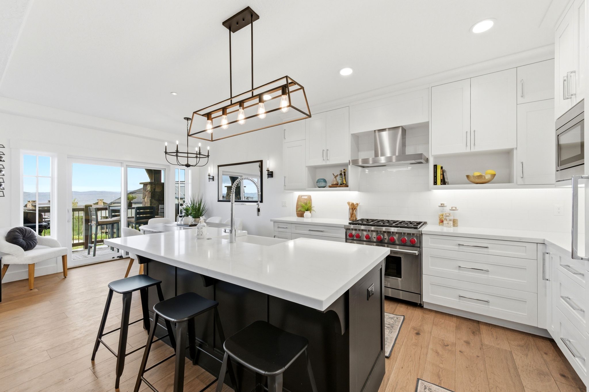Modern kitchen featuring a large central island with seating, white shaker-style cabinetry, stainless steel appliances, and light wood-finish flooring