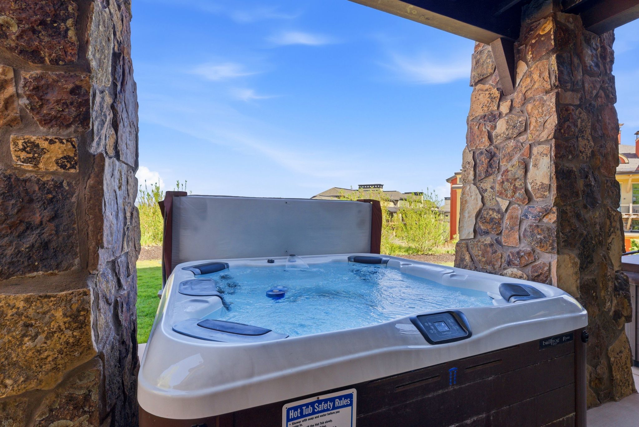 Outdoor spa tub on a stone patio, featuring natural stone pillars and a partial privacy screen