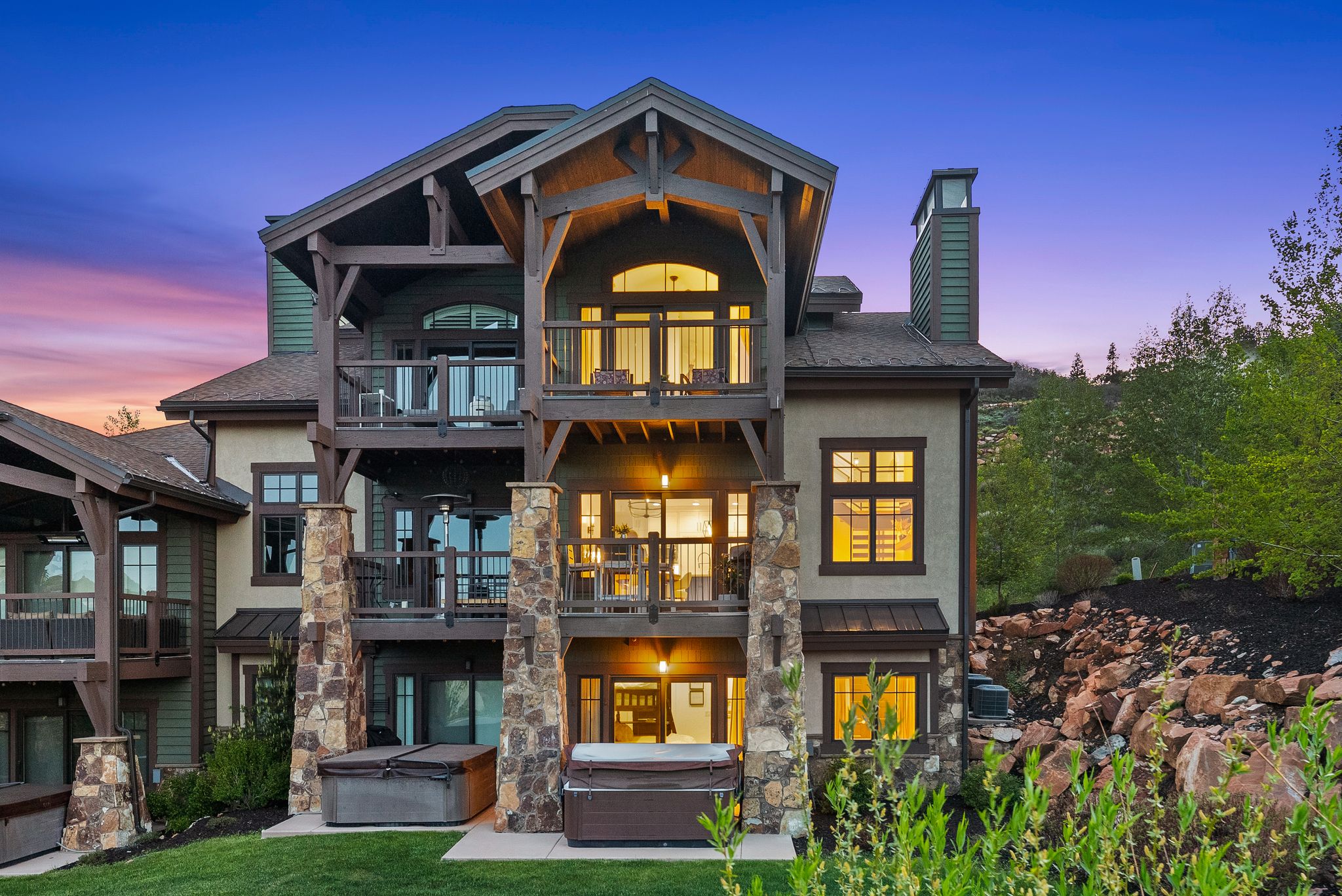 Multi-level residence featuring substantial stone columns, exposed timber beam accents, multiple private balconies, and two built-in hot tubs