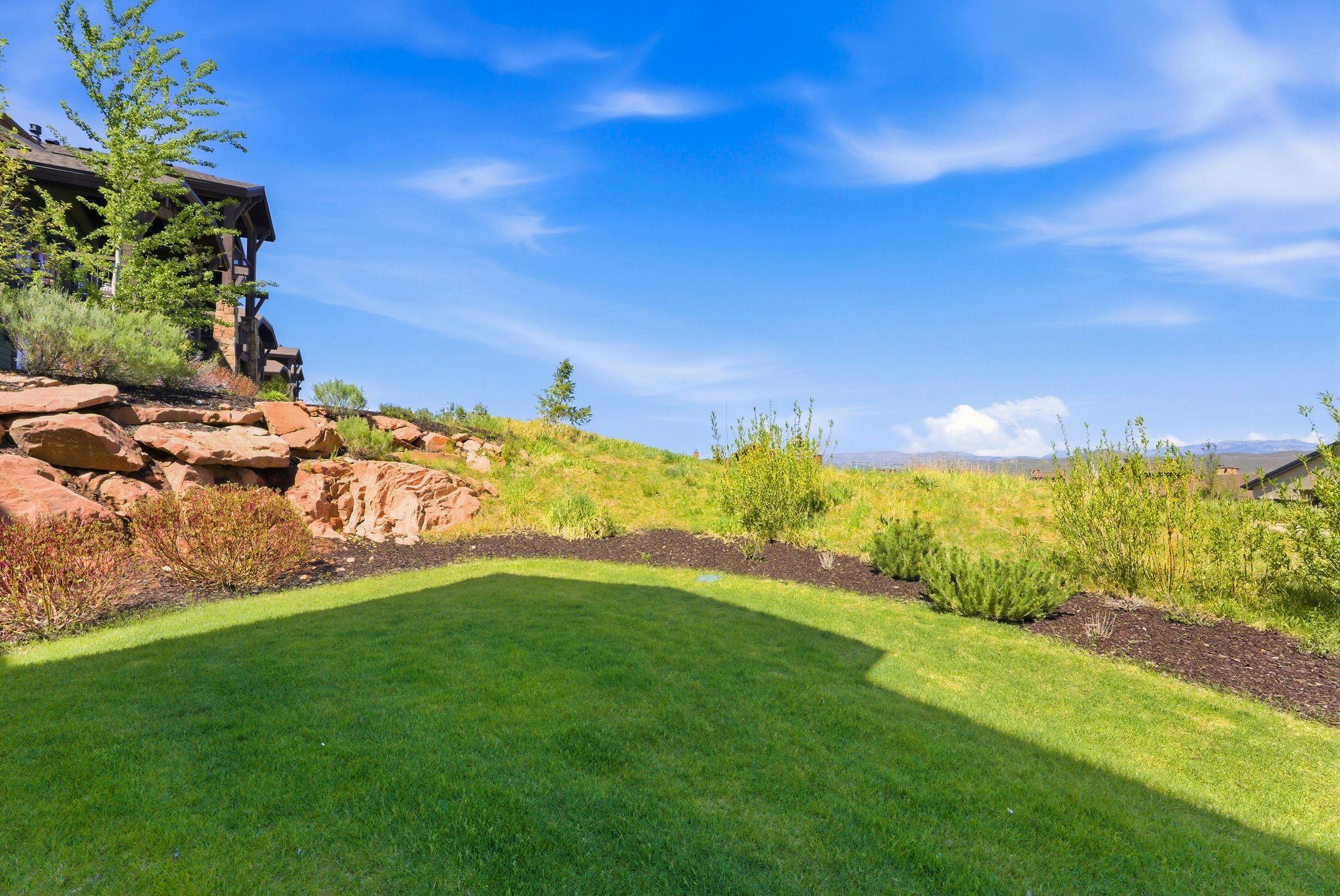 Expansive lawn area with a natural rock retaining wall and mature landscaping