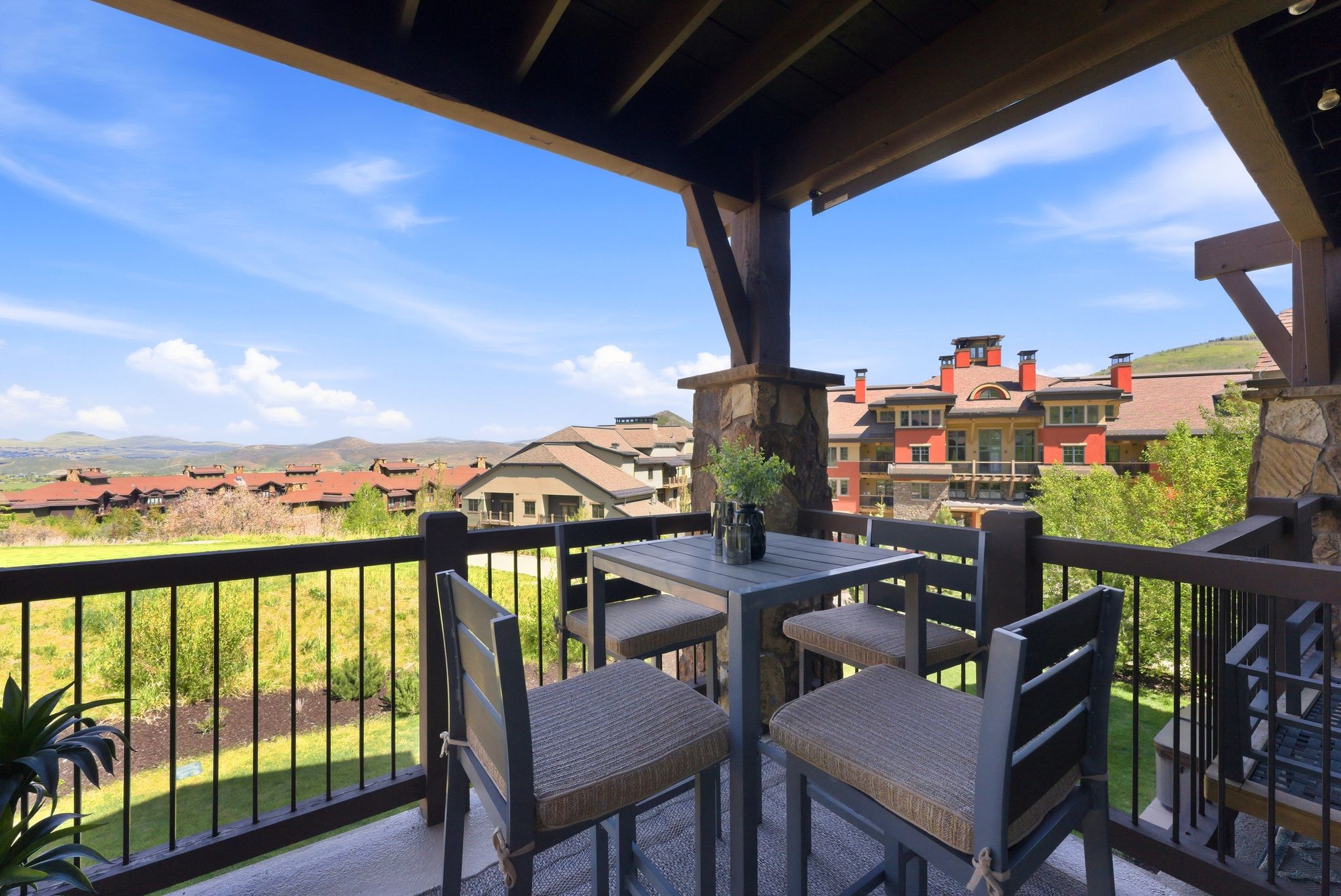 Covered outdoor patio featuring stone column supports, dark wood beam ceiling, and a black metal railing