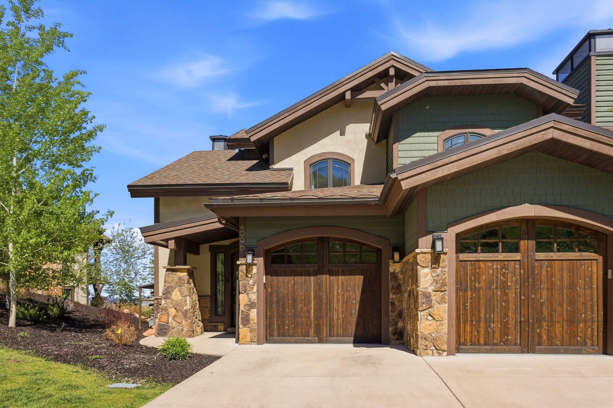 Crafted architectural exterior featuring wood-finish garage doors with arched windows, stone accents, and varied siding