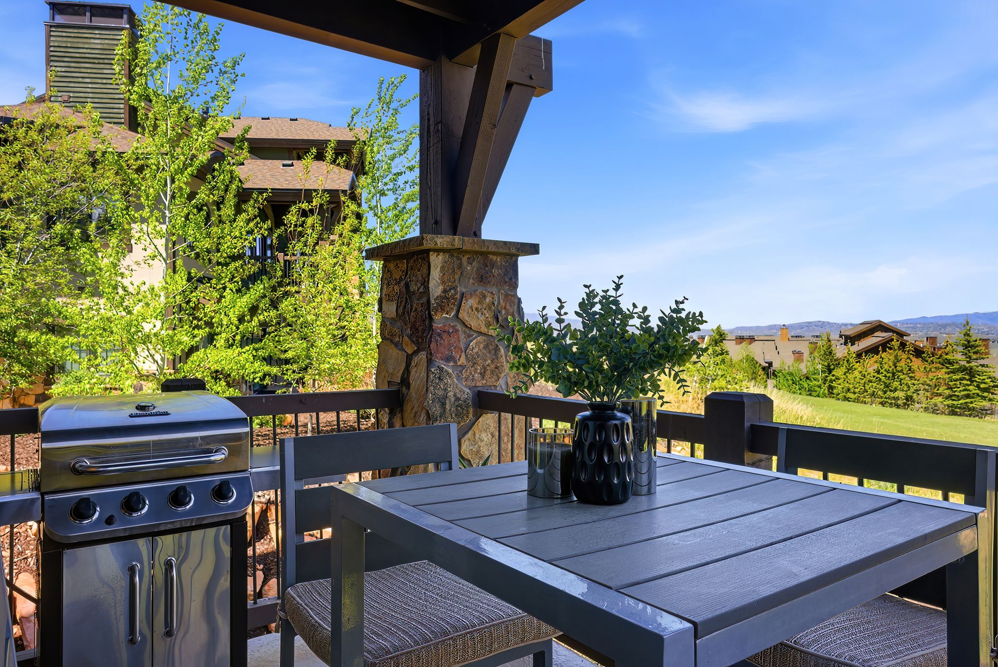 Outdoor patio featuring a stone-clad support column, dark-stained wooden beams, and a slatted patio table