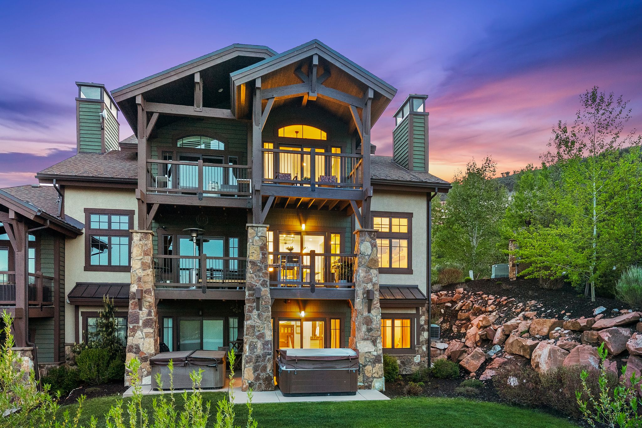 Multi-level residence featuring stone and stucco exterior, multiple private balconies, and a ground-level patio with two built-in hot tubs