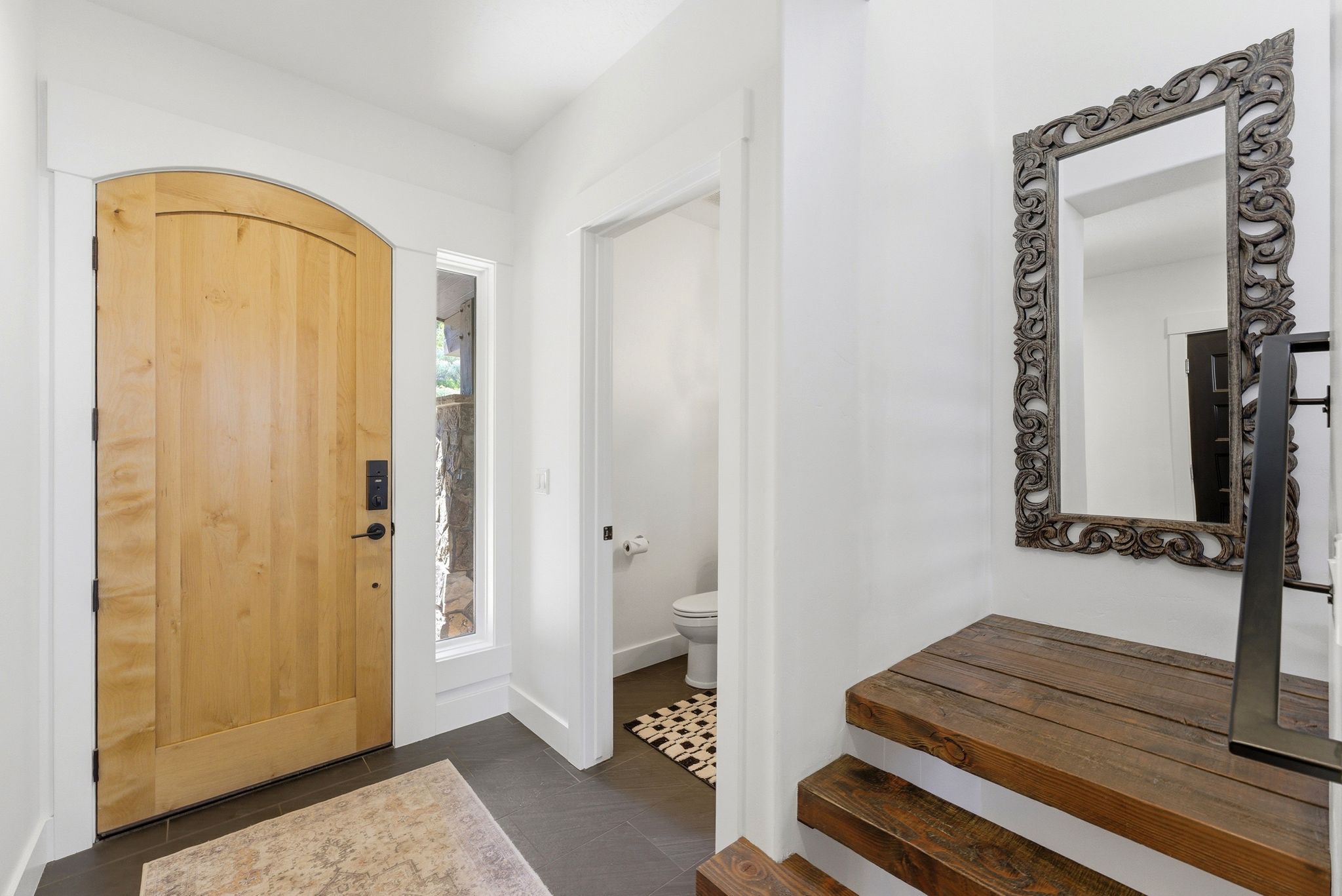 Arched wood entry door with vertical sidelight, dark tile flooring, and white trim
