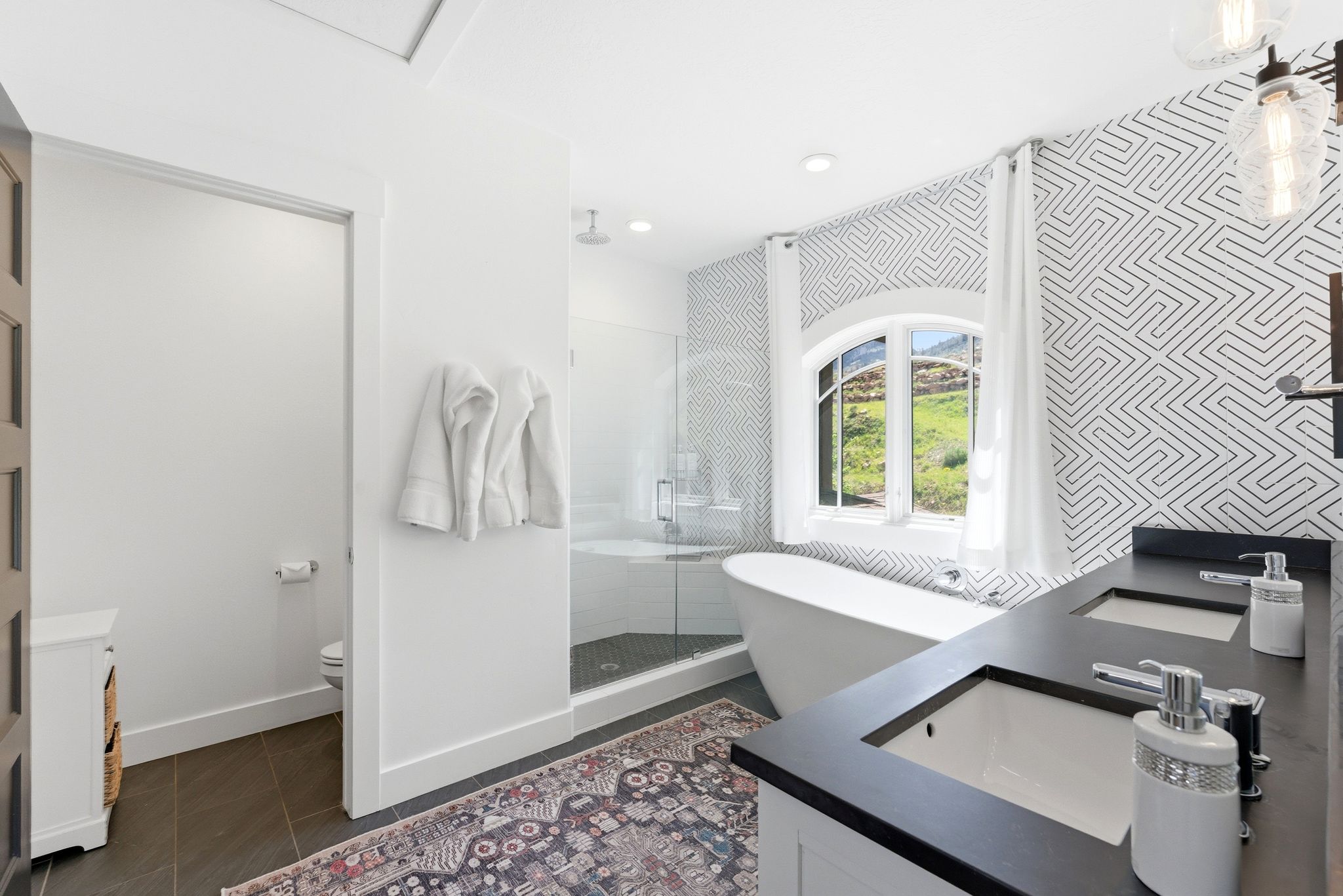 Spacious bathroom featuring a freestanding tub, glass-enclosed shower, dual vanity with undermount sinks, and patterned accent wall tiling